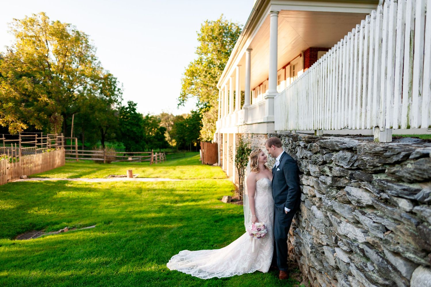 Wedding photos captured against rustic stone wall and white fence during golden hour.