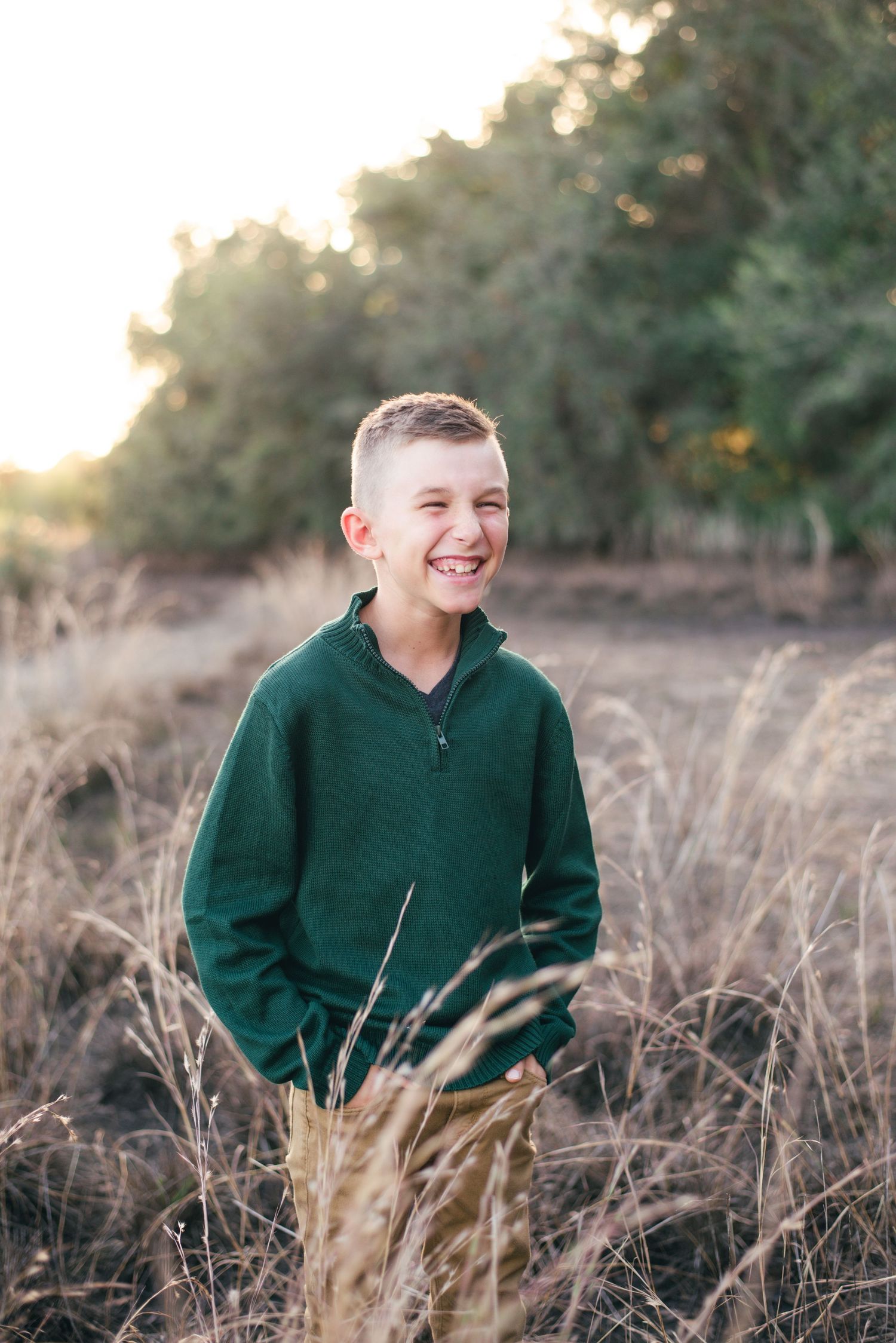 Portrait series of a young person in a dark green sweater sitting in autumn field at sunset.