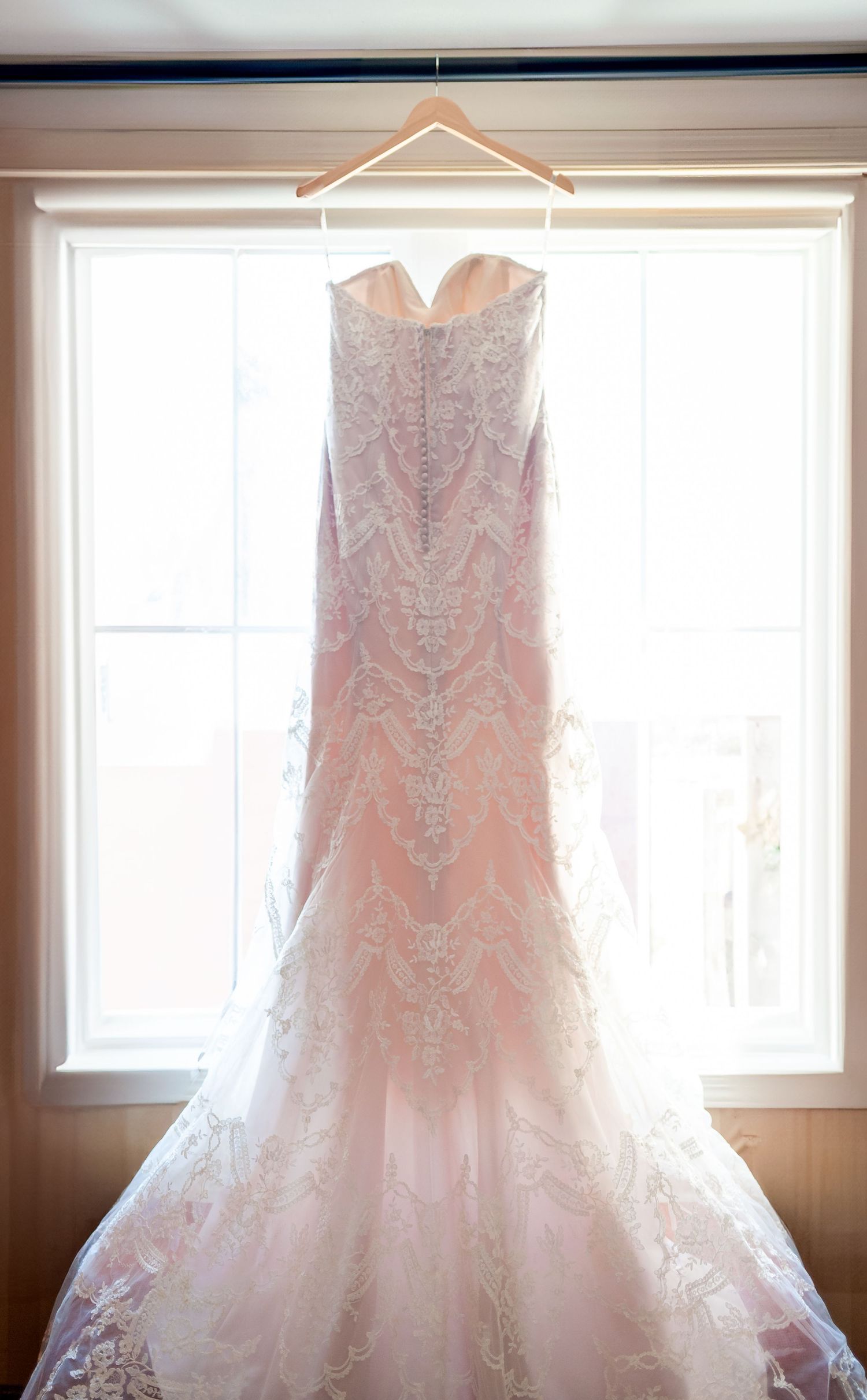Elegant lace wedding dress with fitted bodice and flared skirt hanging in window light.