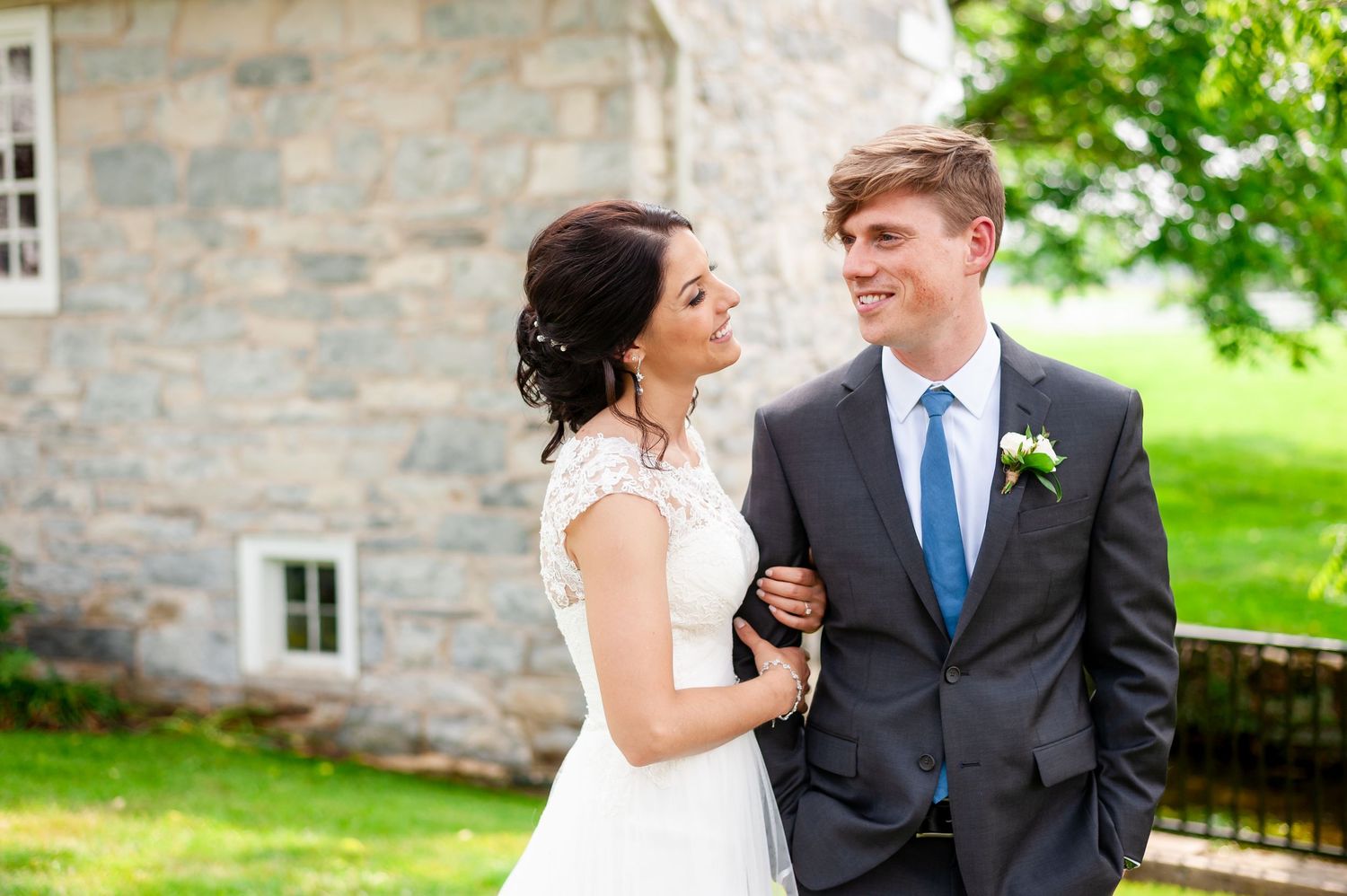 Elegant wedding couple laughing together in front of historic stone building.