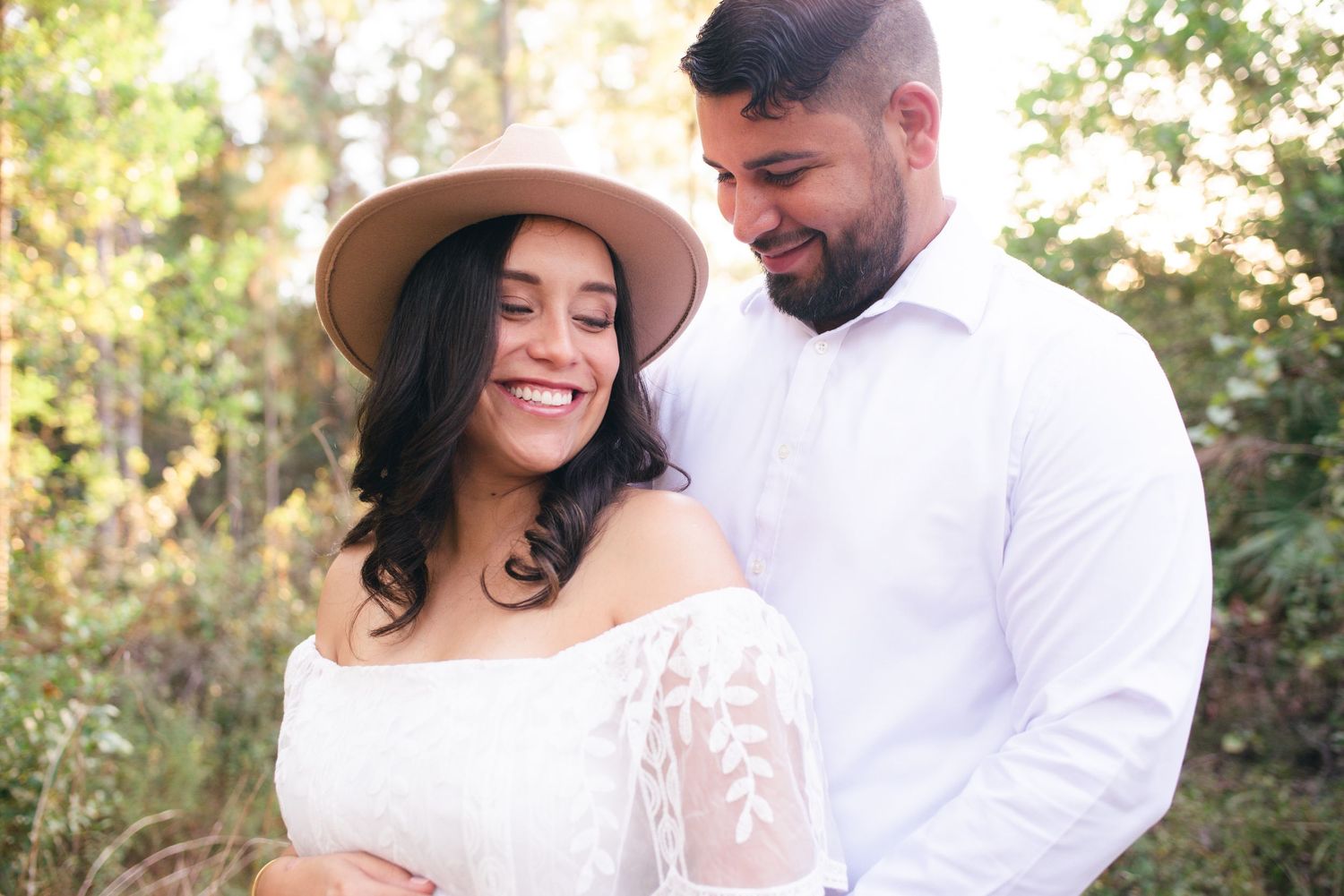 A couple in light-colored clothing shares tender moments during an outdoor photo session at sunset.