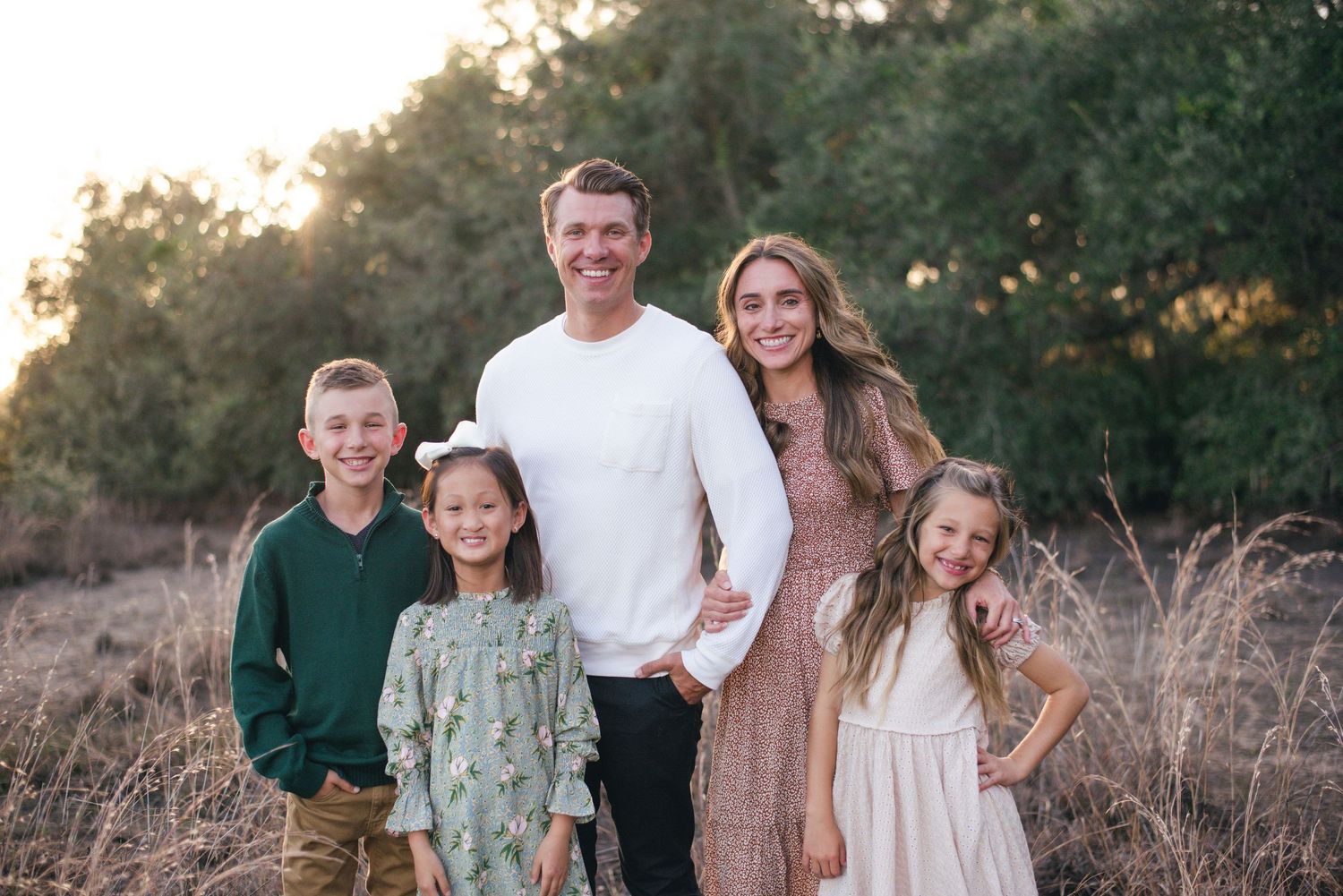 Family of five poses together outdoors at sunset in a natural field setting.