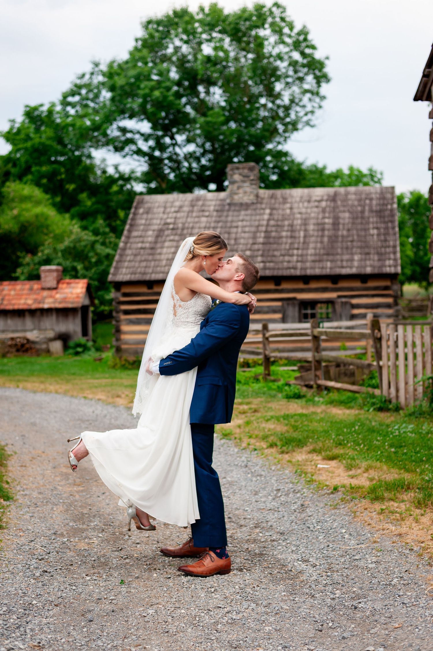 Romantic wedding lift pose on a gravel path with rustic log cabin in the background.
