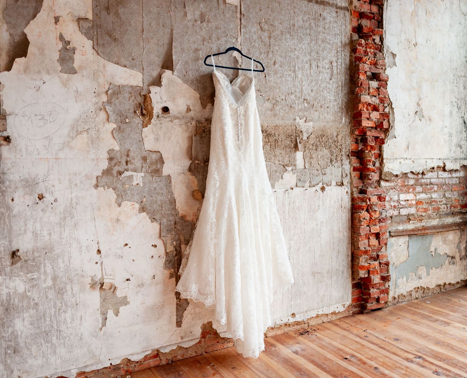 White wedding dress hanging on display against distressed brick and plaster wall.