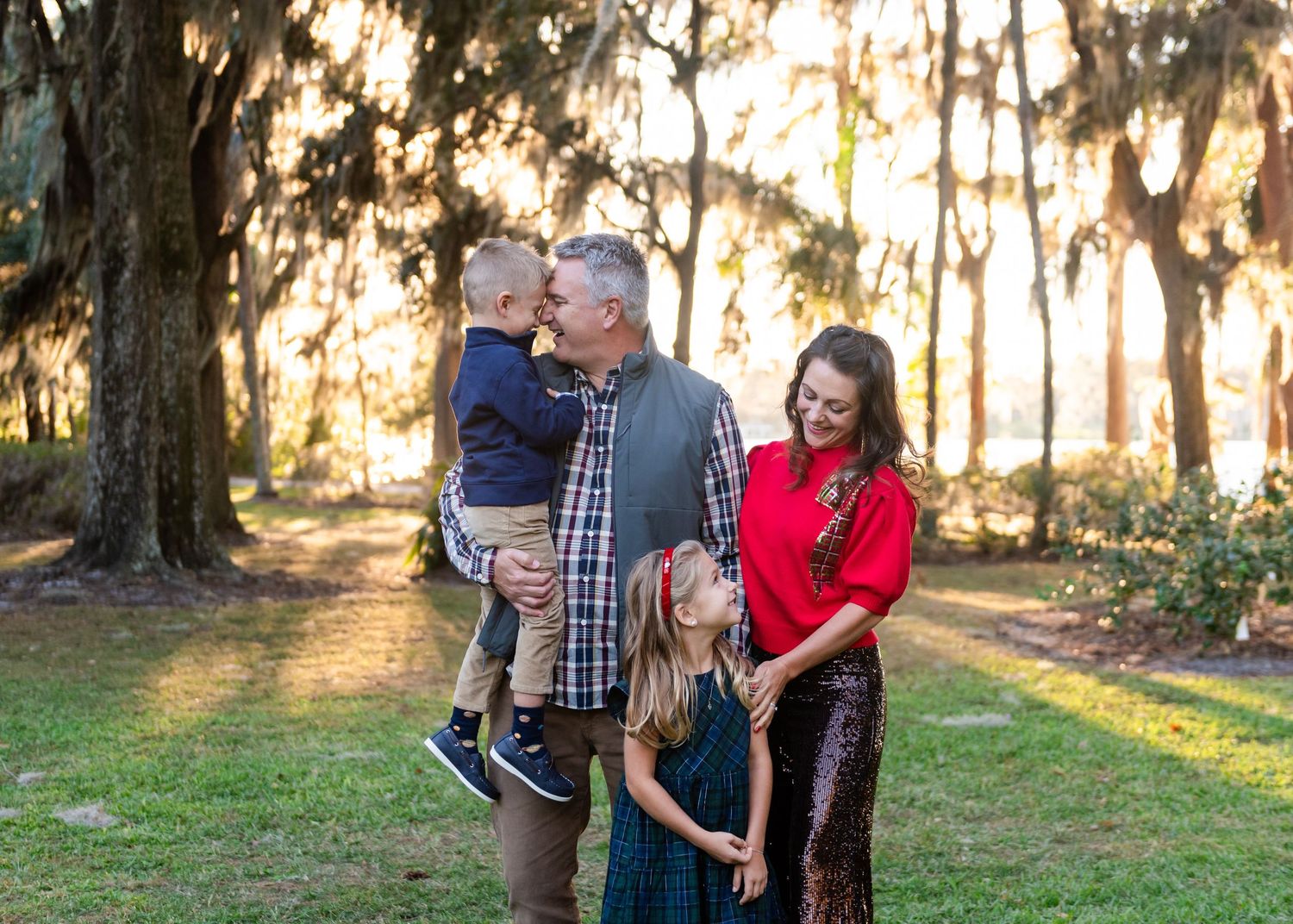 Family dressed in coordinating casual outfits walking and laughing together during golden hour in a park.