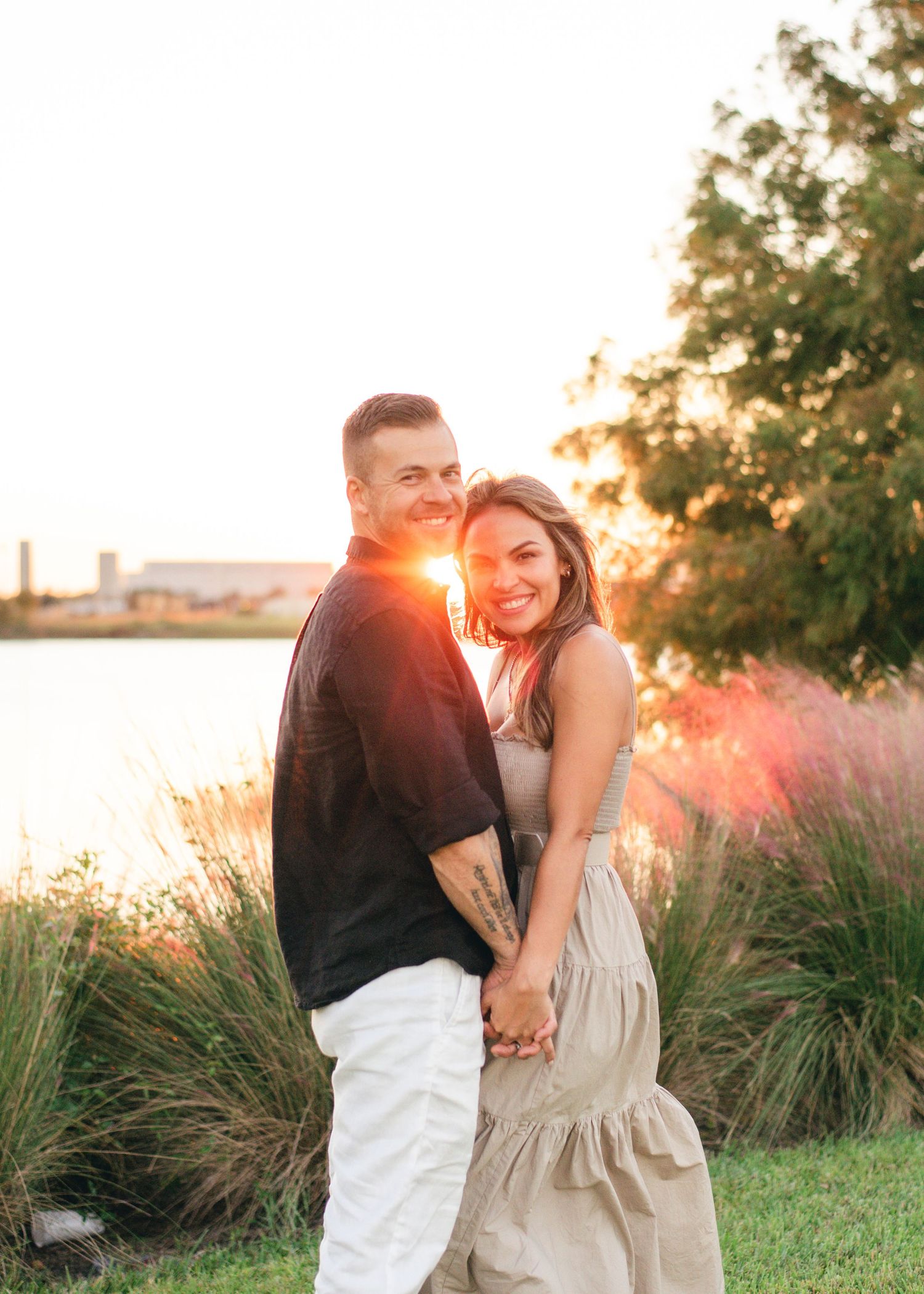 Romantic couple holding hands and laughing together during golden hour by the water.