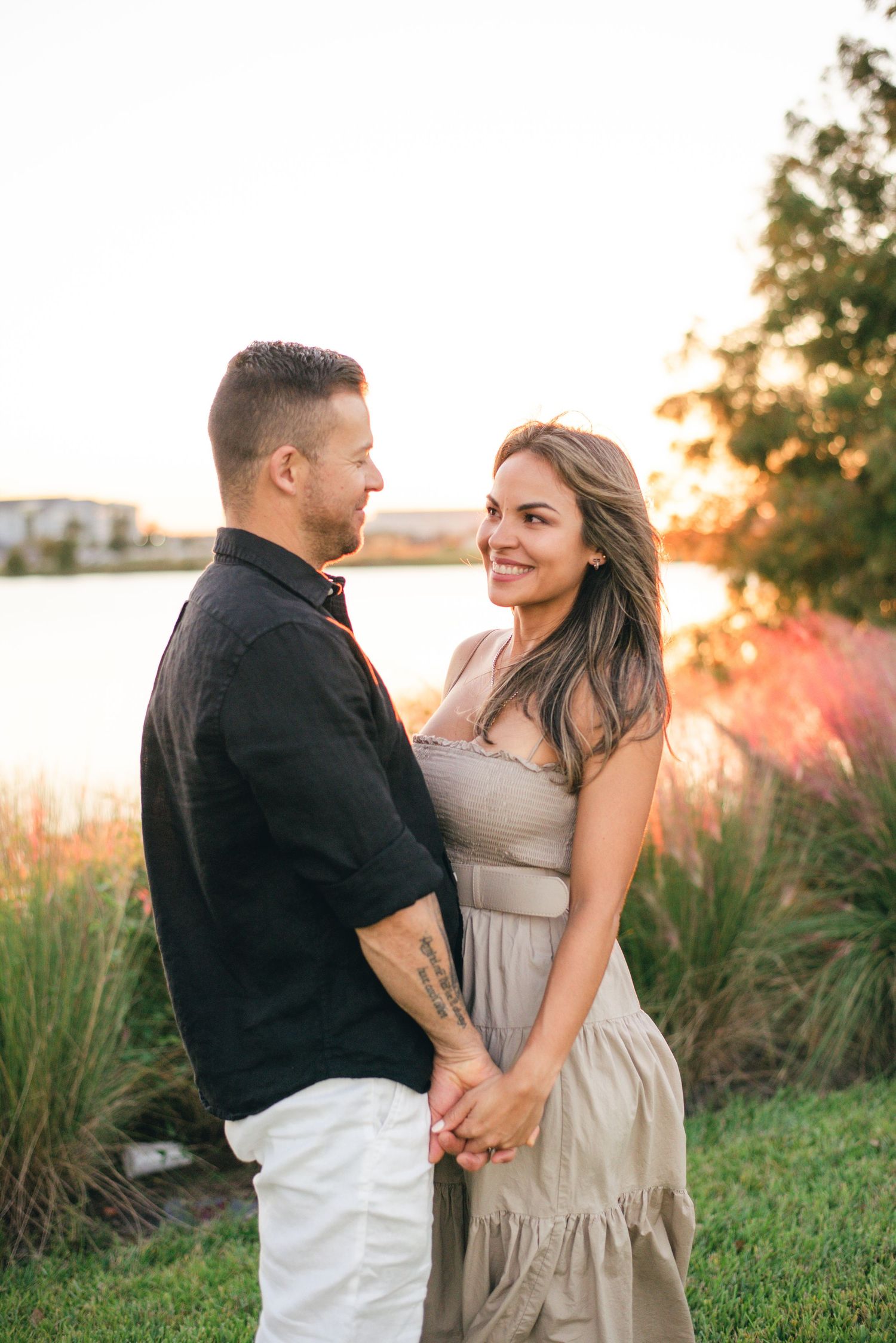 A couple shares a romantic moment together outdoors during sunset with tall grass and nature in the background.