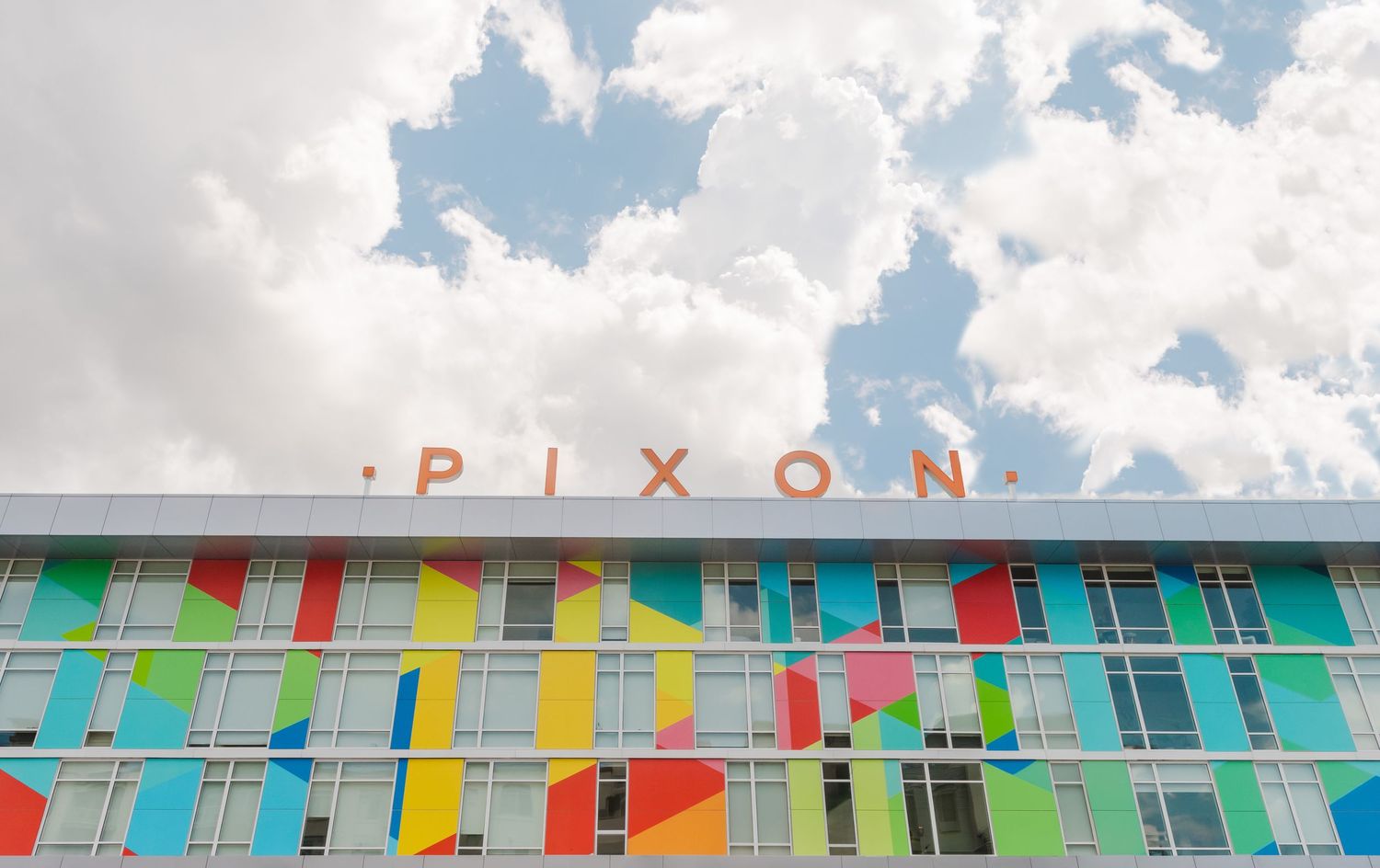 A colorful retro motel exterior with Pixon signage features vibrant geometric patterns painted across its facade.