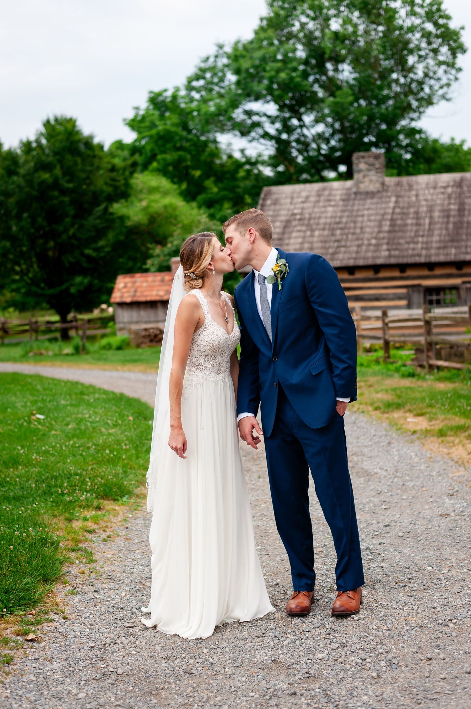 Wedding couple shares intimate moment on gravel path with rustic log cabin setting.
