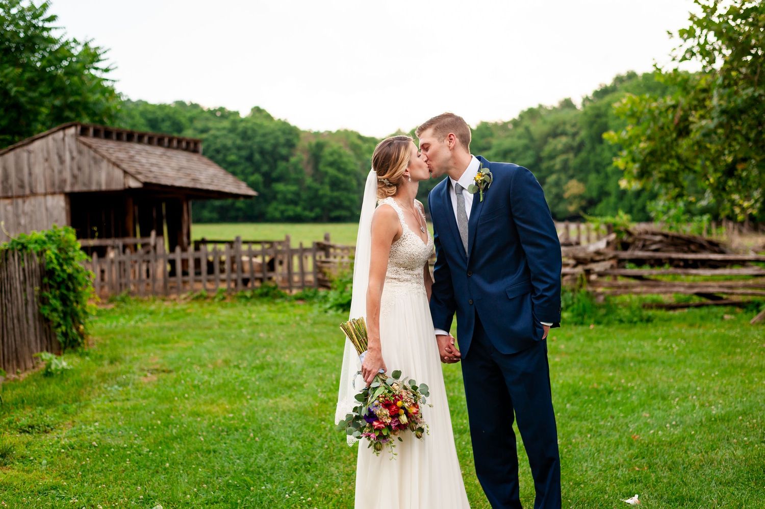 Wedding couple embraces in front of rustic wooden barn structure.