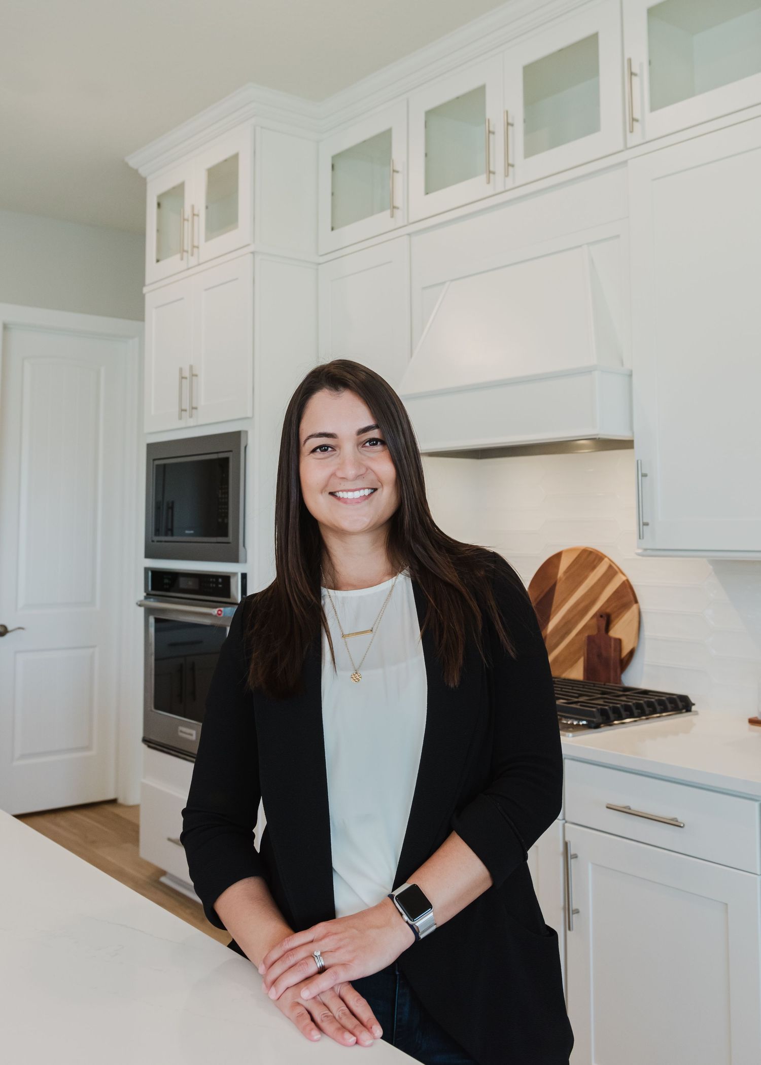 Professional wearing black blazer and white top seated in bright modern kitchen.