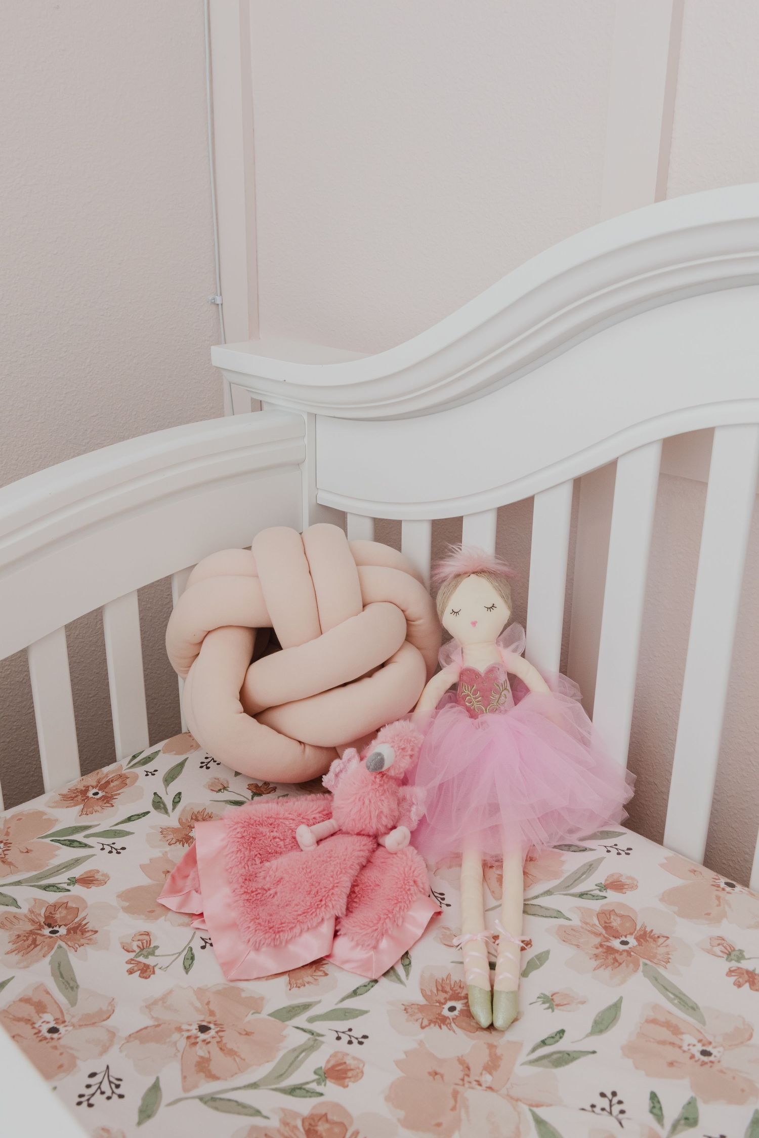 White crib with pink floral bedding and plush toys creating cozy nursery atmosphere.