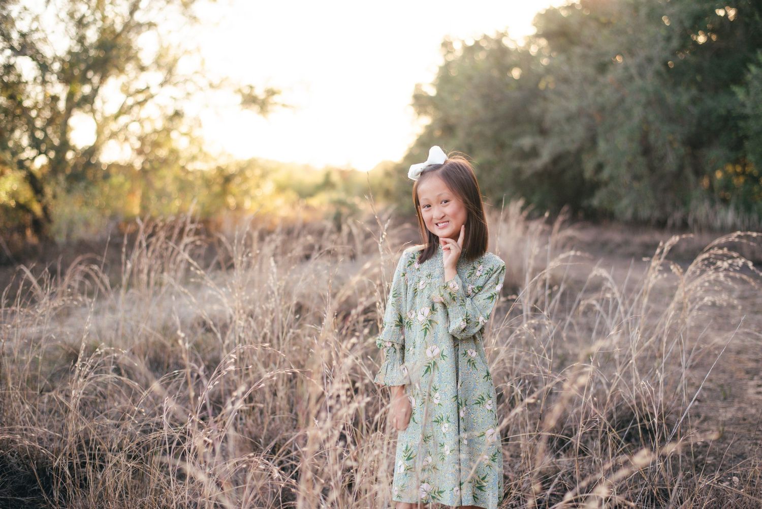 Someone in a mint green dress stands in a golden sunlit field of tall grass during sunset.