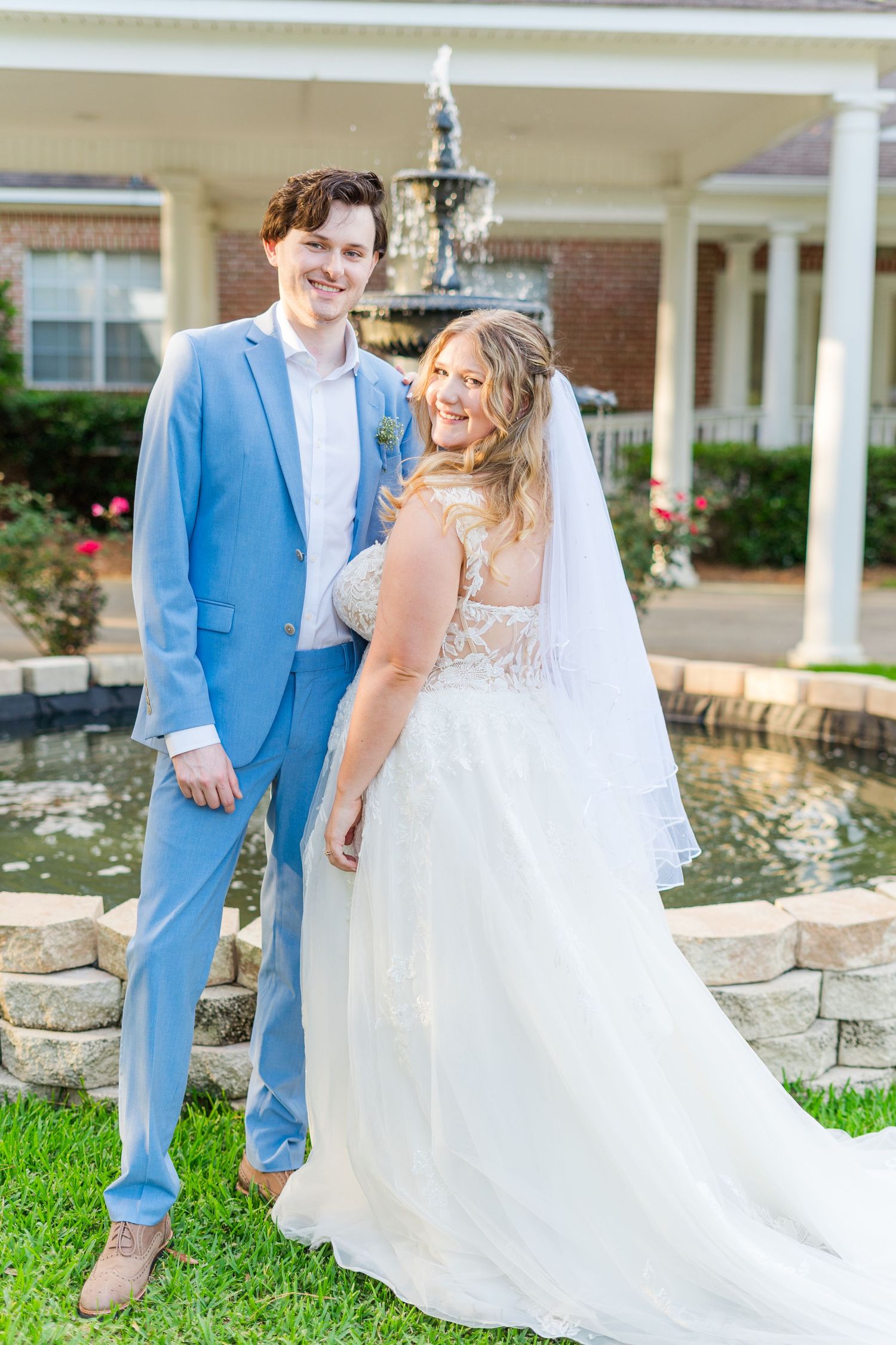 Wedding couple in blue and white attire posing by stone wall and white columns.