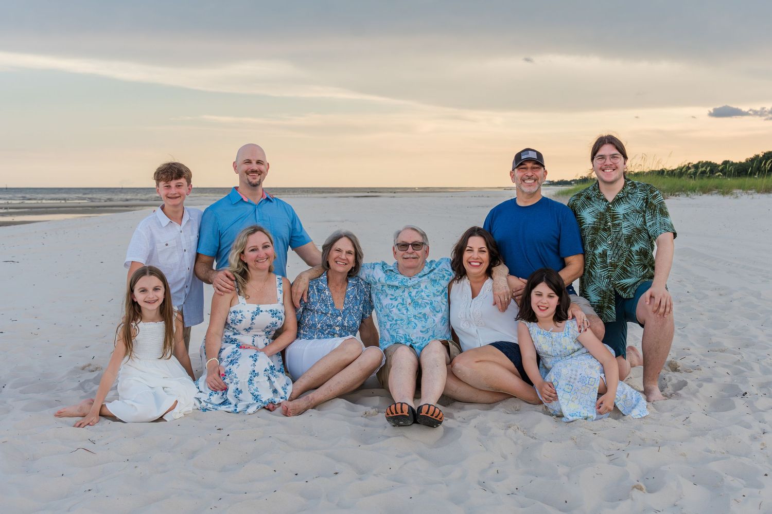 Extended family members sitting together on white sand beach during sunset photography session.