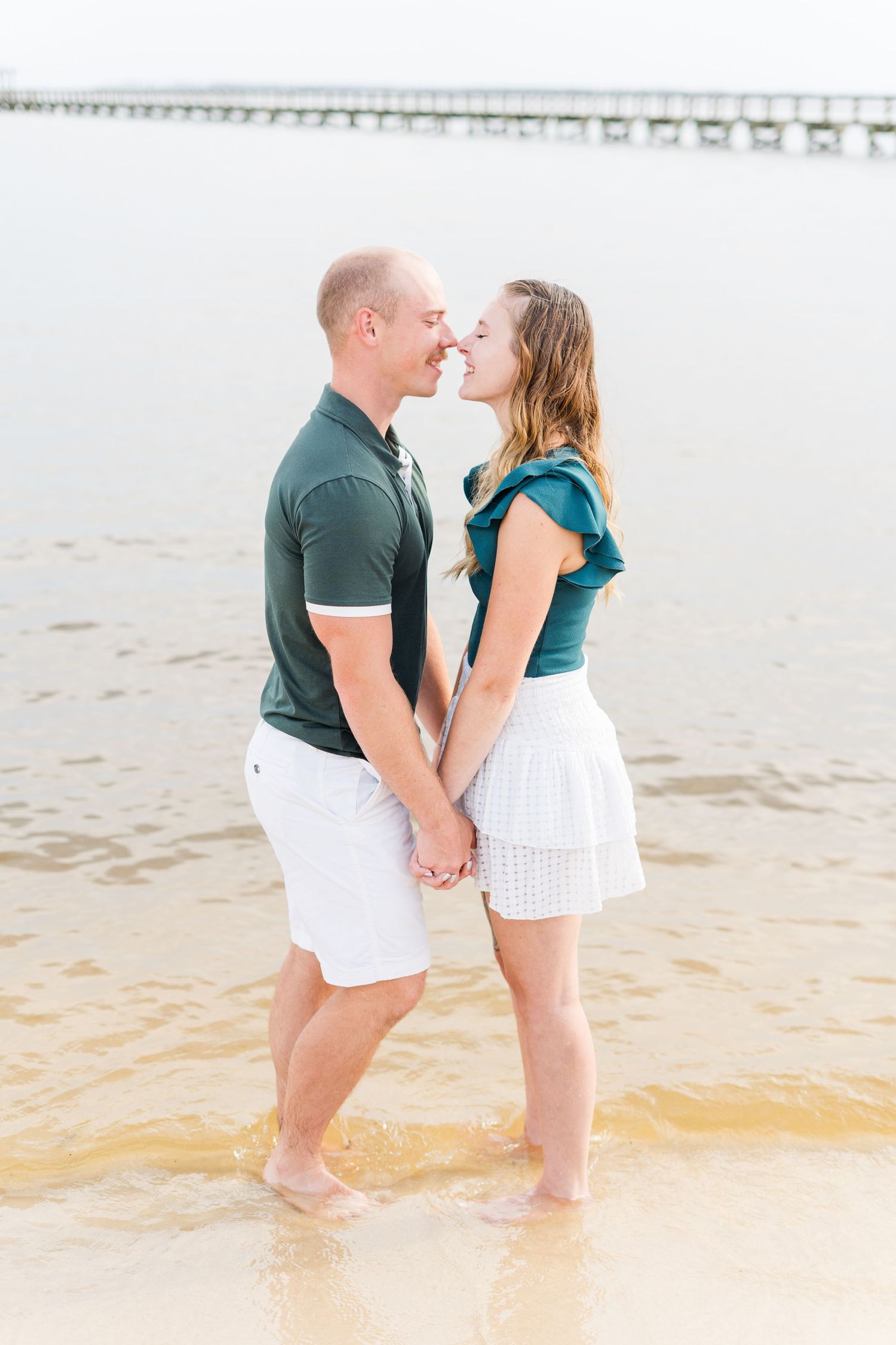 A couple in coordinating outfits shares an intimate moment at the beach during sunset.