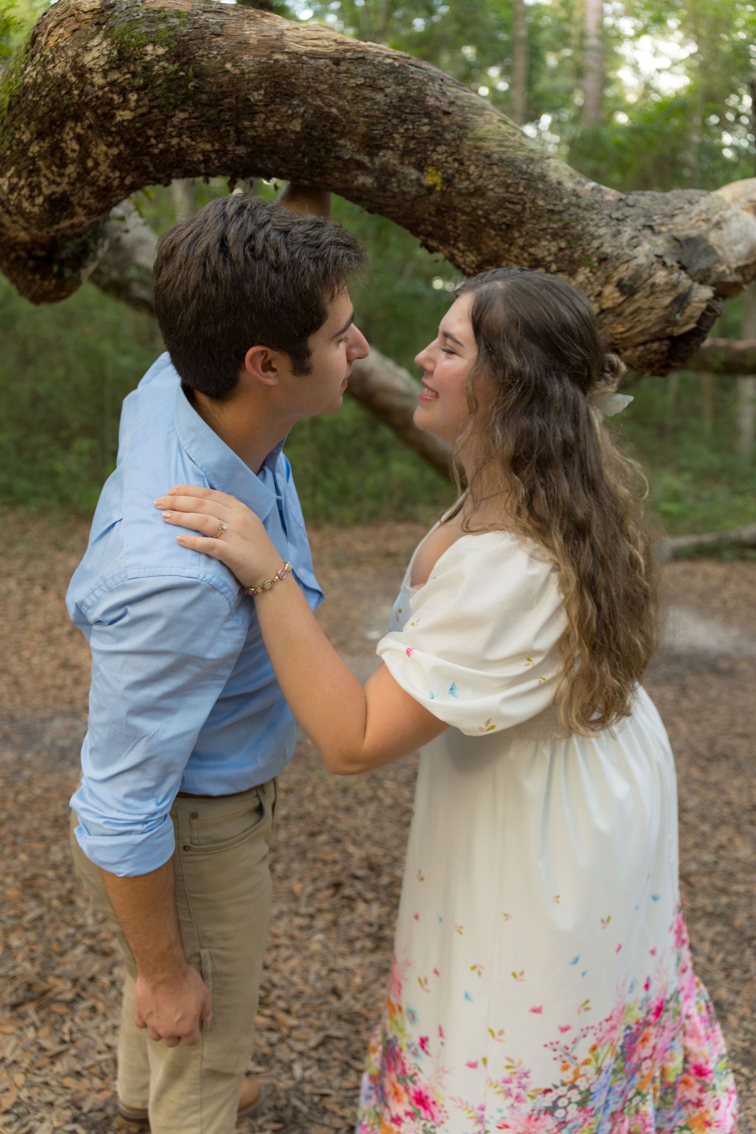 A couple shares intimate moments under a curved tree branch during their engagement shoot.