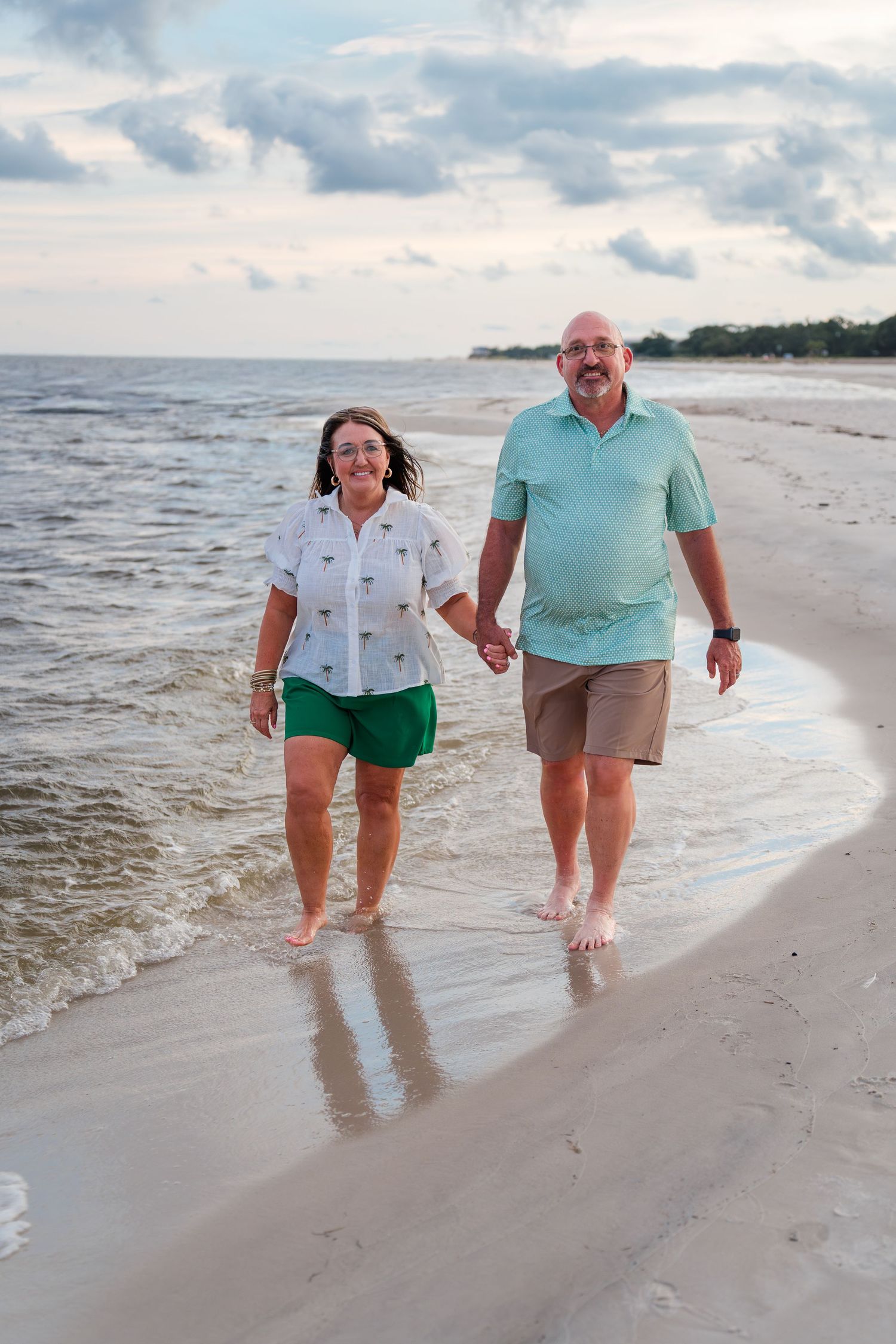 A couple takes a romantic stroll along the beach shoreline during sunset, leaving footprints in the wet sand.
