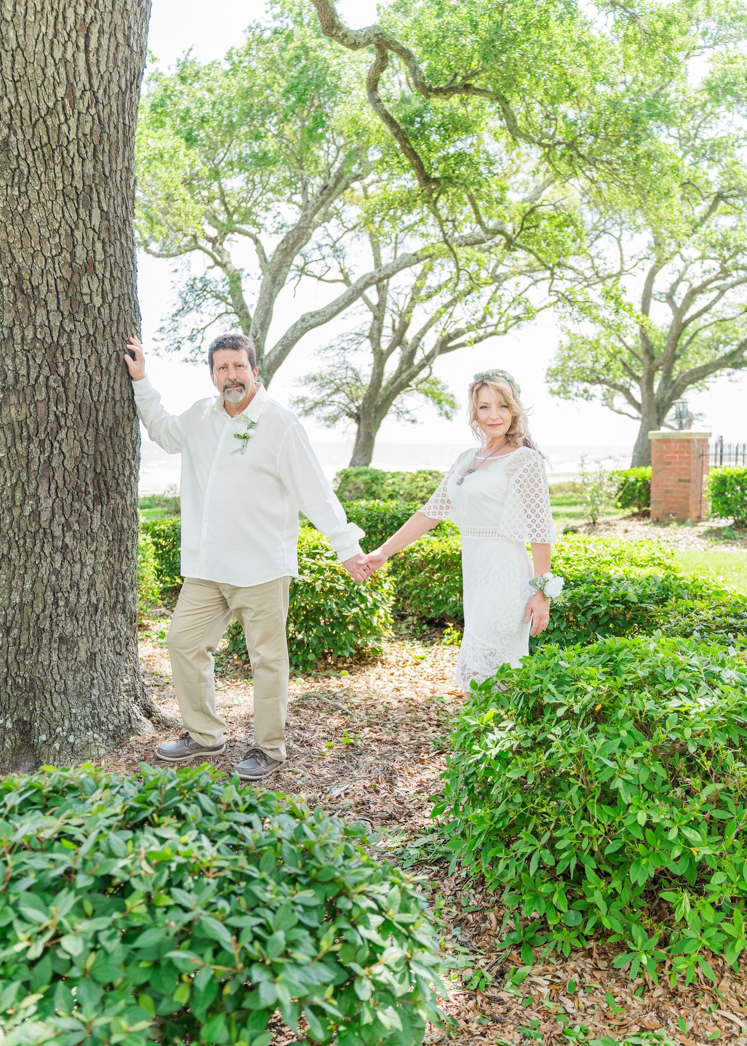 Romantic garden wedding portraits with couple in white outfits among trees and greenery.