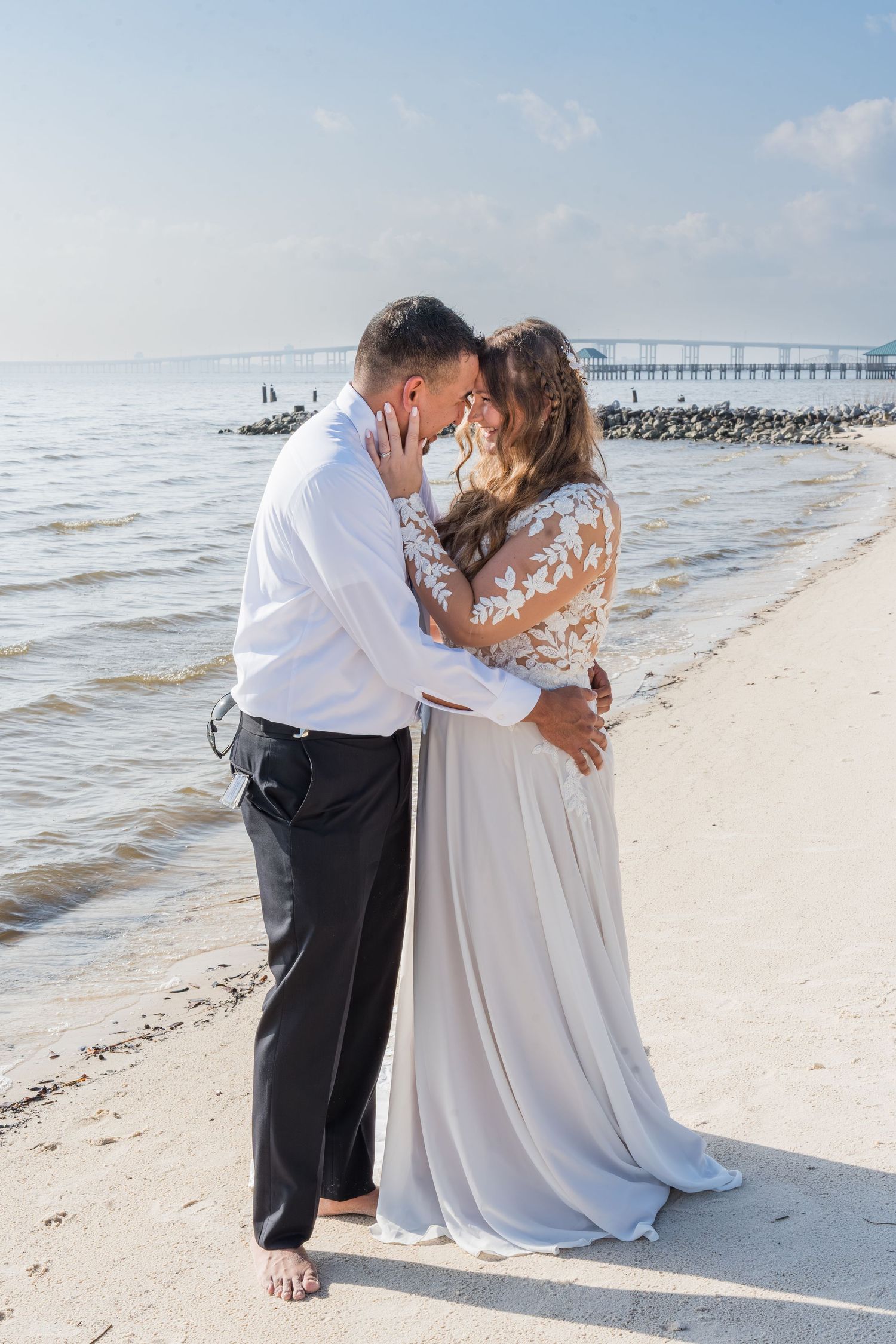 A romantic couple shares tender moments on a sandy beach with a wooden pier in the background.