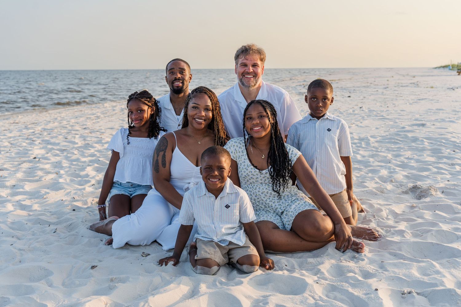 Family group enjoying candid moments together during beach photo shoot at sunset.