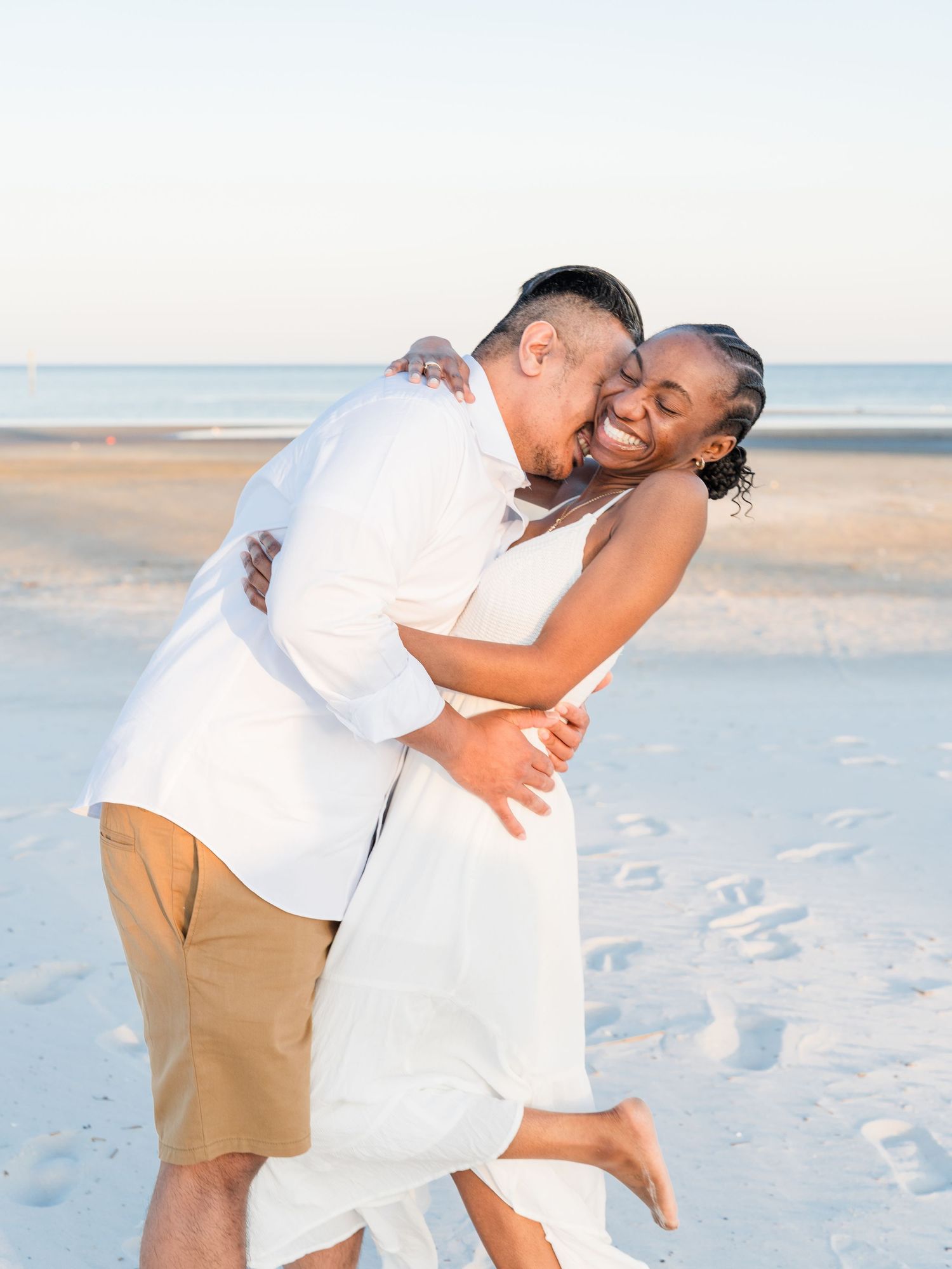 A joyful couple shares playful moments on a bright white sandy beach during a photo session.