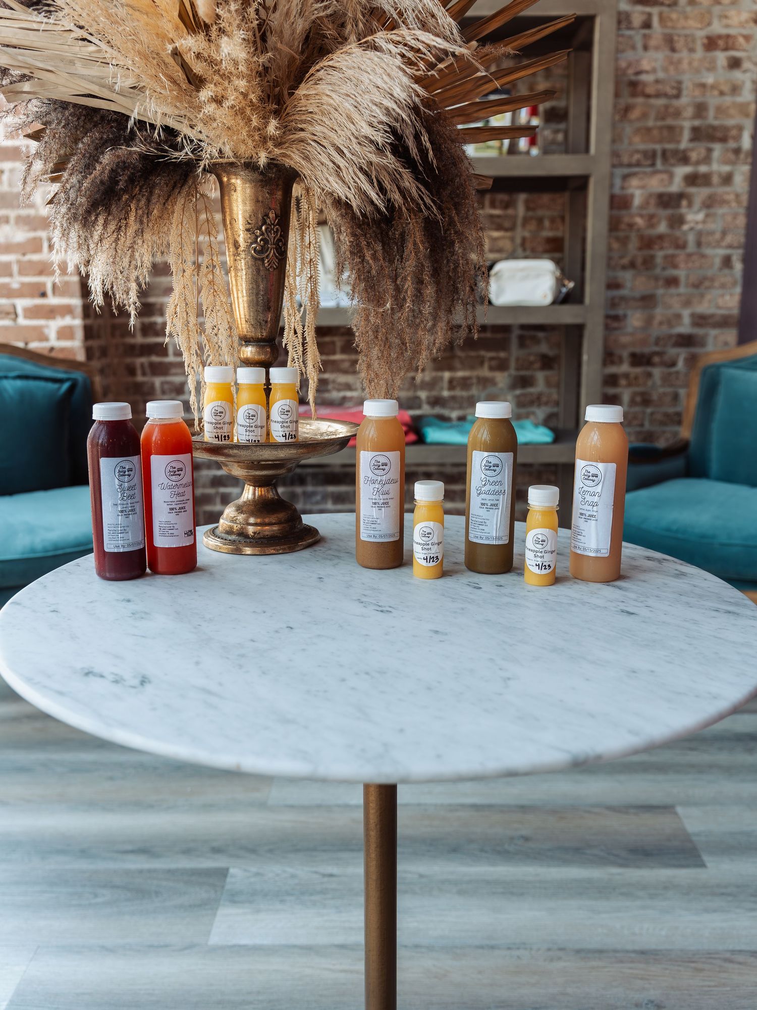 Artisanal bottled beverages arranged on a marble table with decorative dried pampas grass centerpiece.