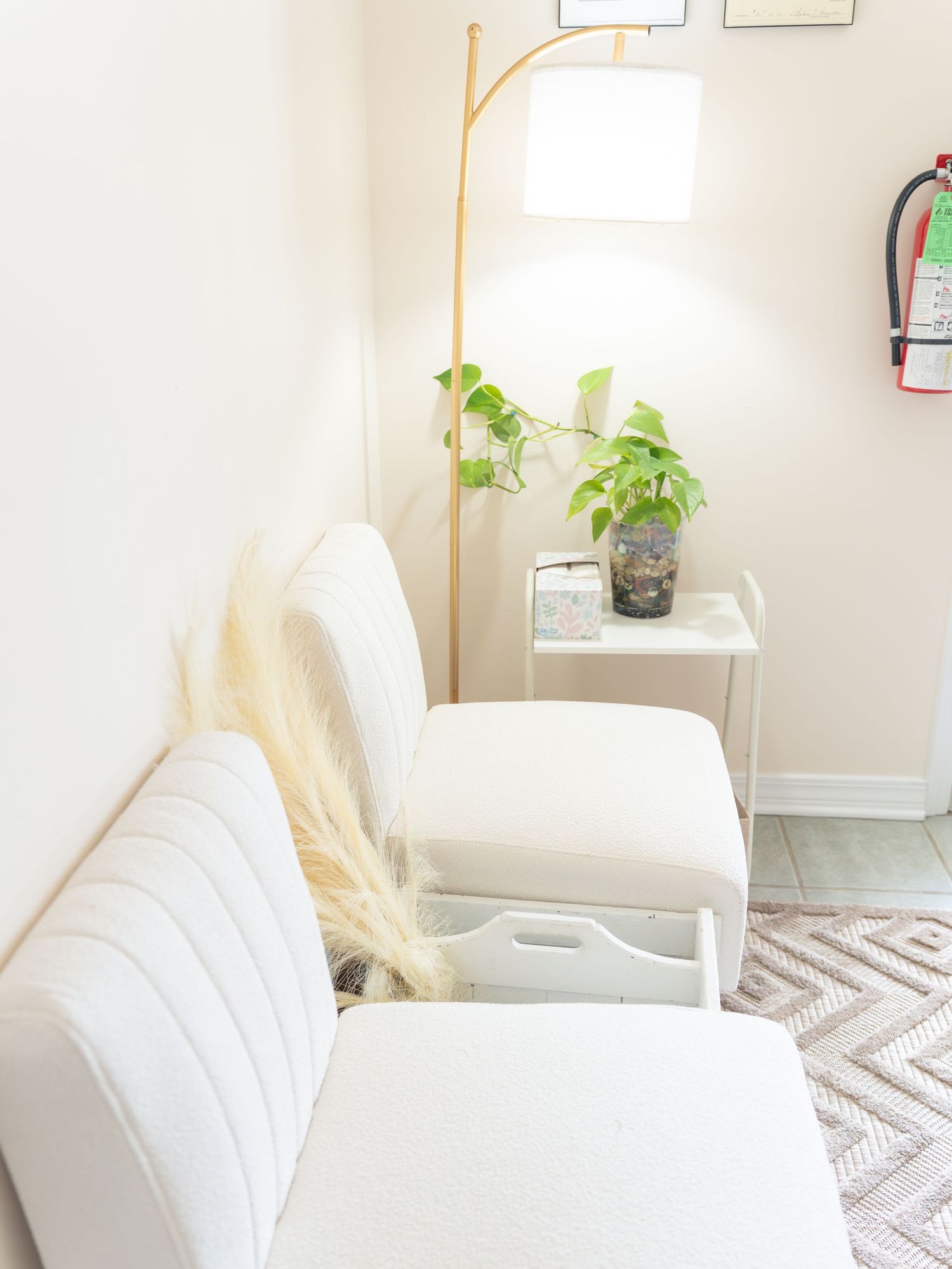 Minimalist living room corner with white furniture, gold lamp and potted plant.