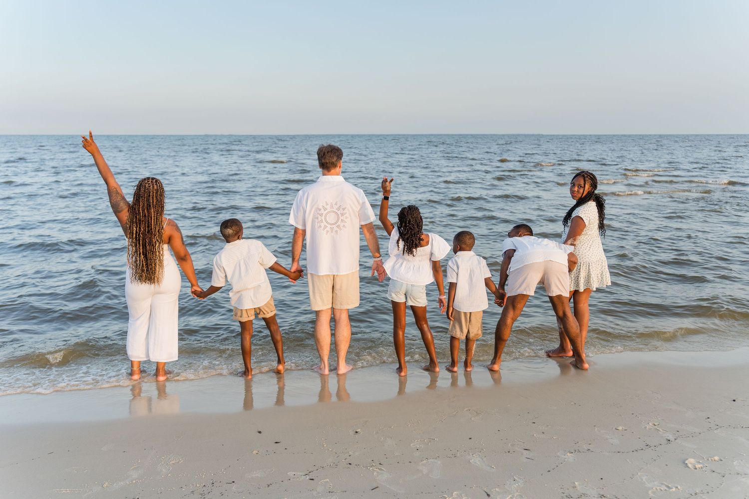 Group portrait of a family wearing white shirts and jeans sitting together on the beach.