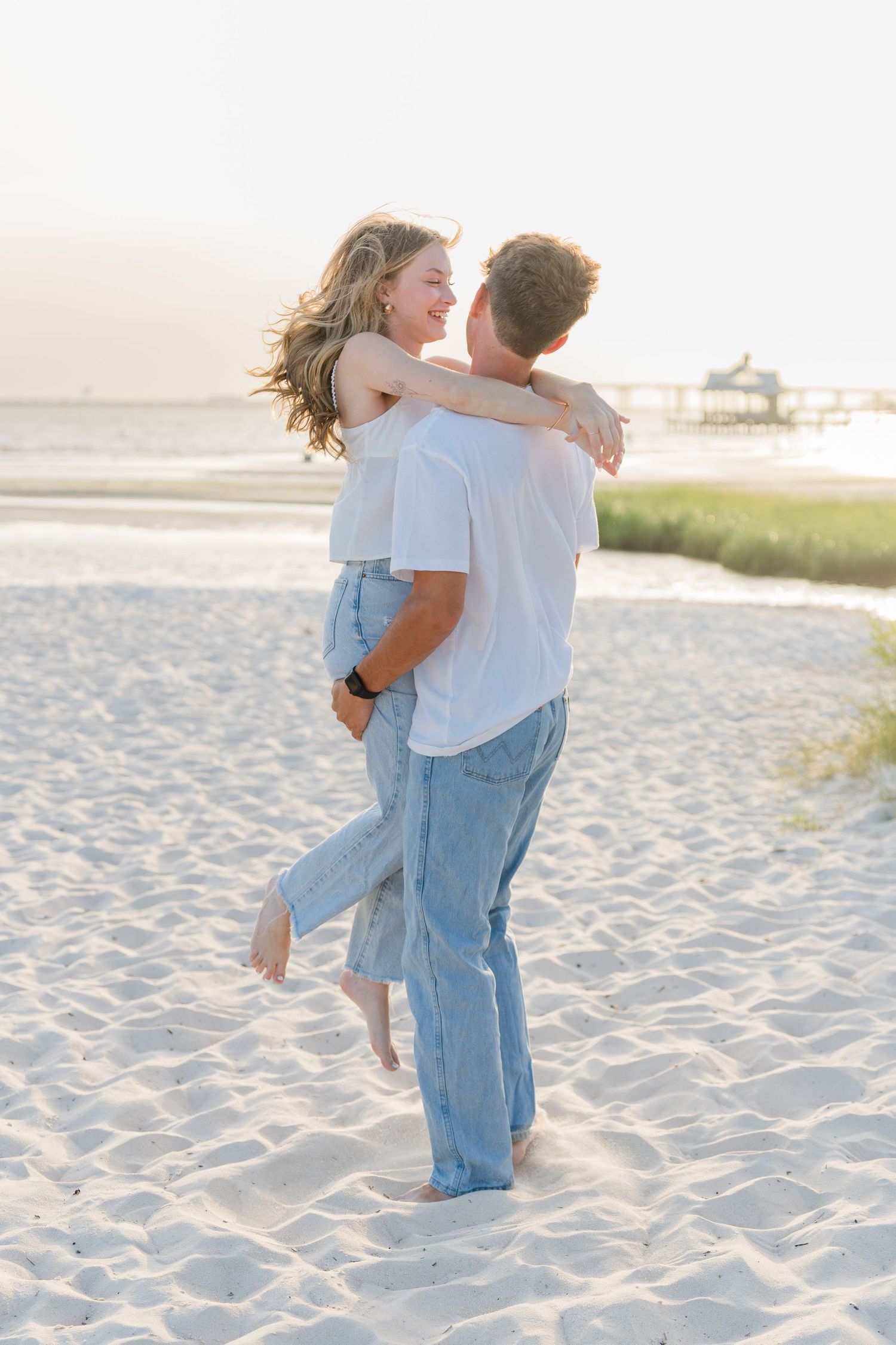 Playful couple hugging and laughing together on a sandy beach at dusk.