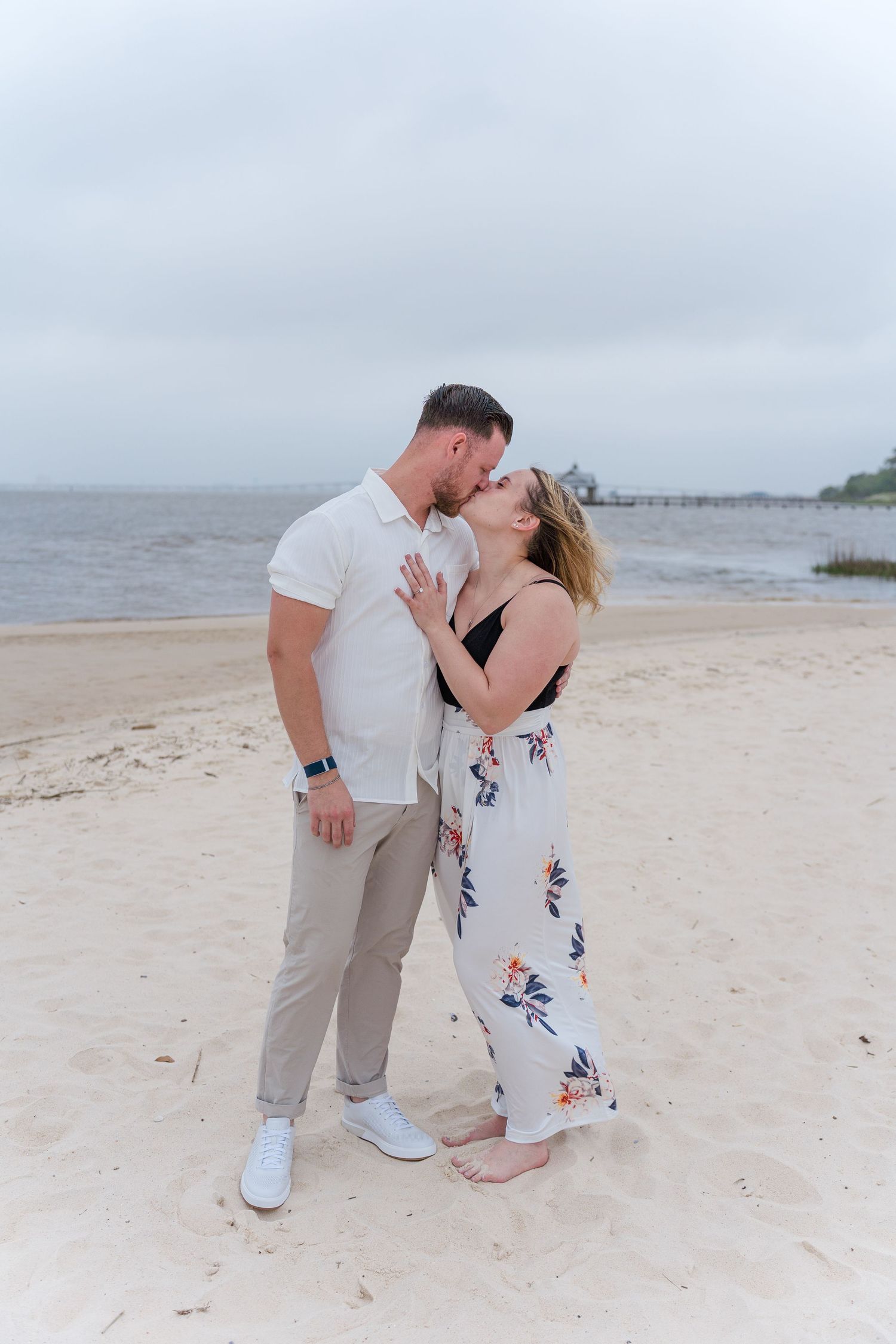 A couple shares their first kiss as engaged partners on a sunny beach.