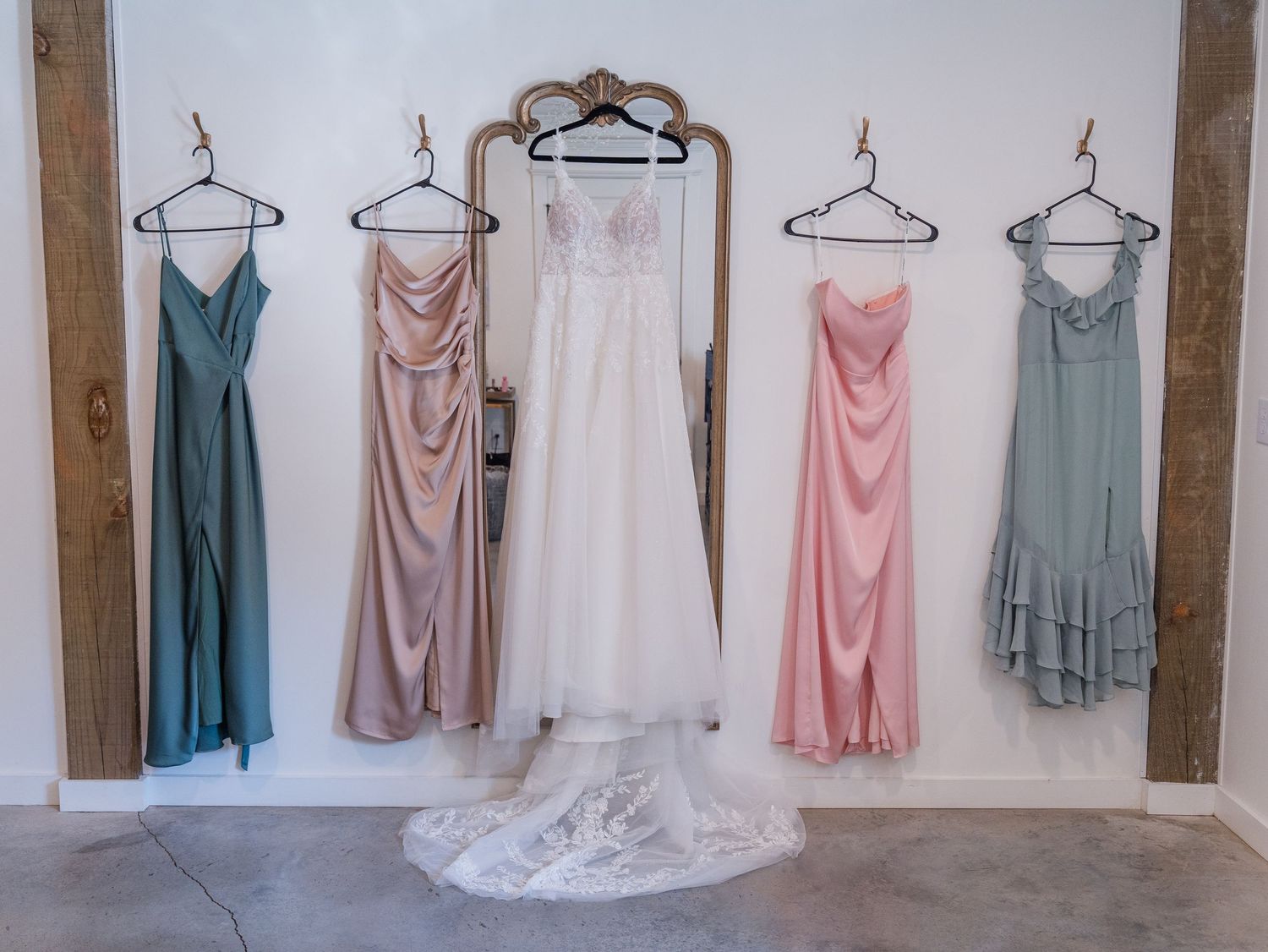 A row of pink, white, and blue bridesmaid dresses hanging on wooden hangers against a rustic wall.