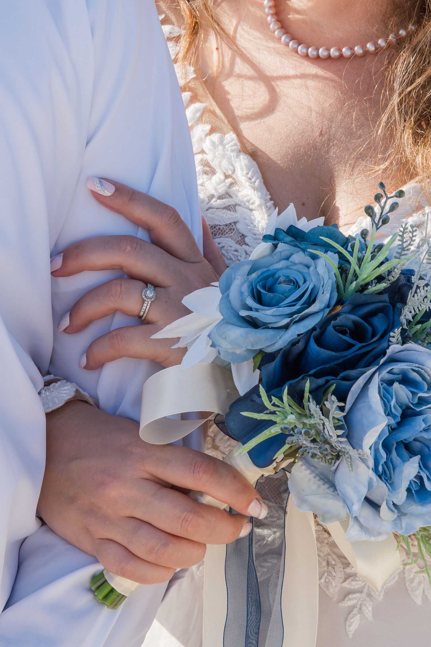A close-up view of hands holding a bridal bouquet with blue roses and white flowers against a white dress.
