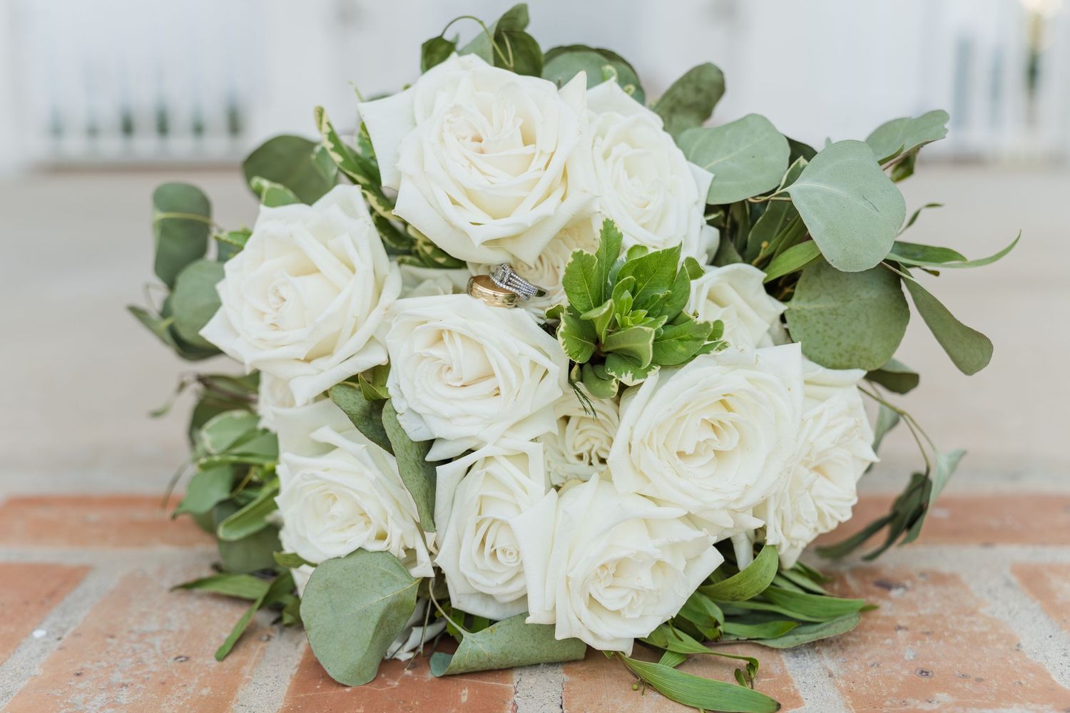 White roses and eucalyptus leaves arranged in an elegant centerpiece vase on a table setting.