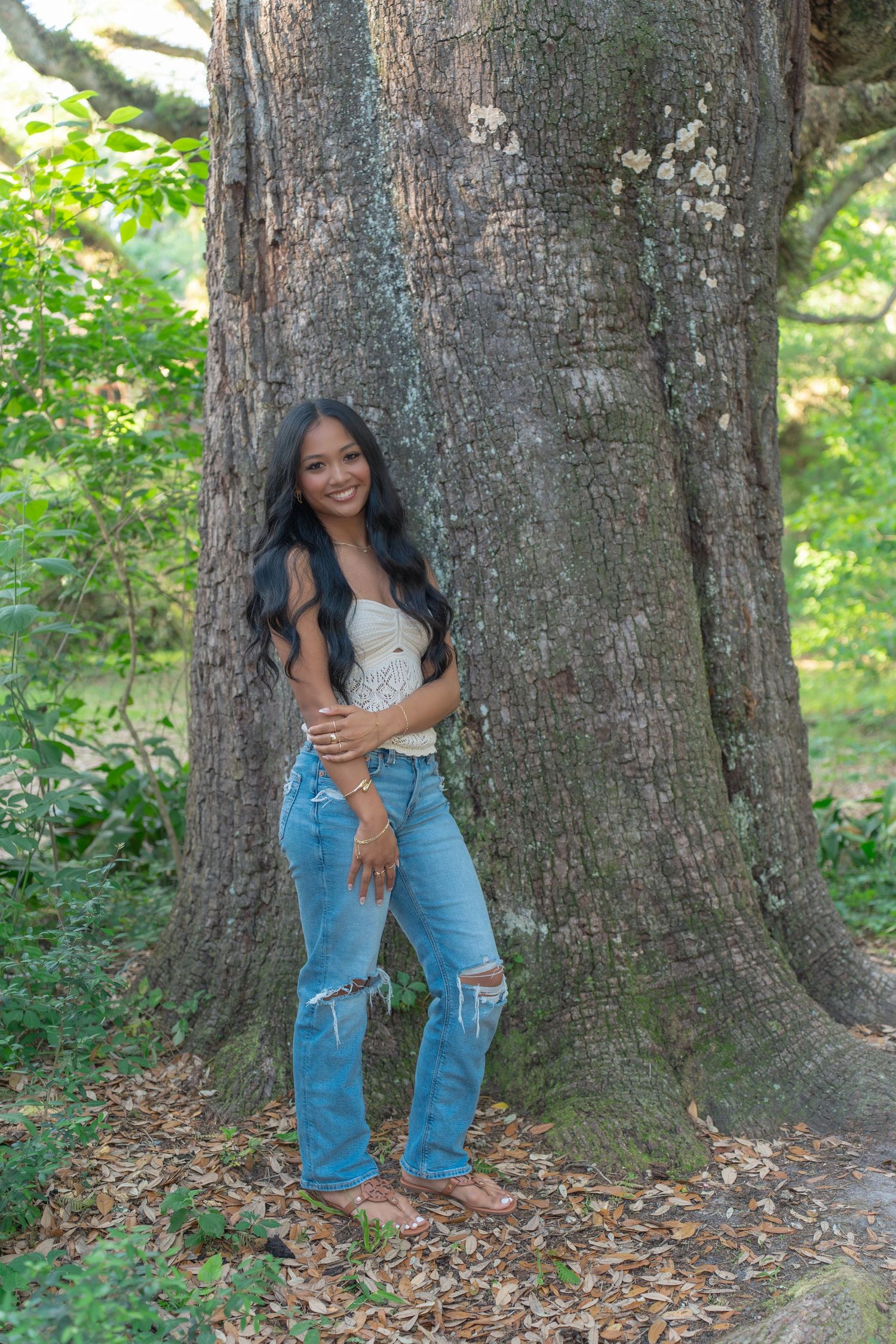 Casual outdoor photo session with distressed jeans and white top against large tree trunk.