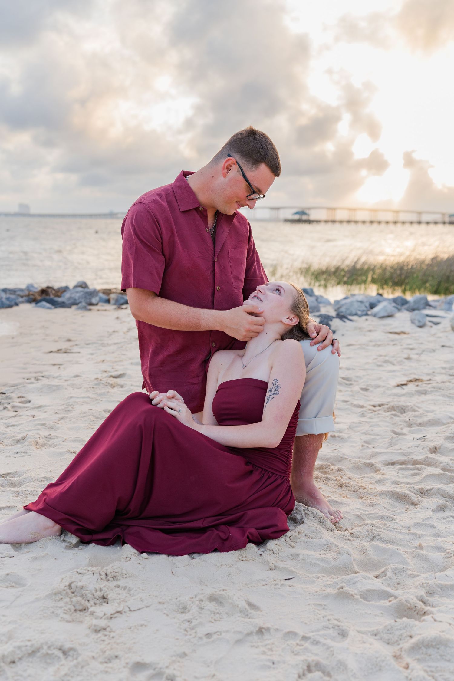 Couple in matching burgundy outfits sharing a romantic moment on a sandy beach at sunset.