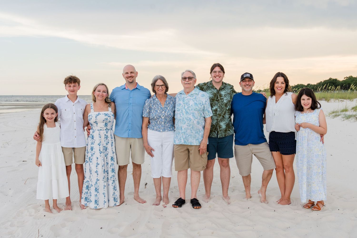 Large family group arranged in casual formation on sandy beach during golden hour.
