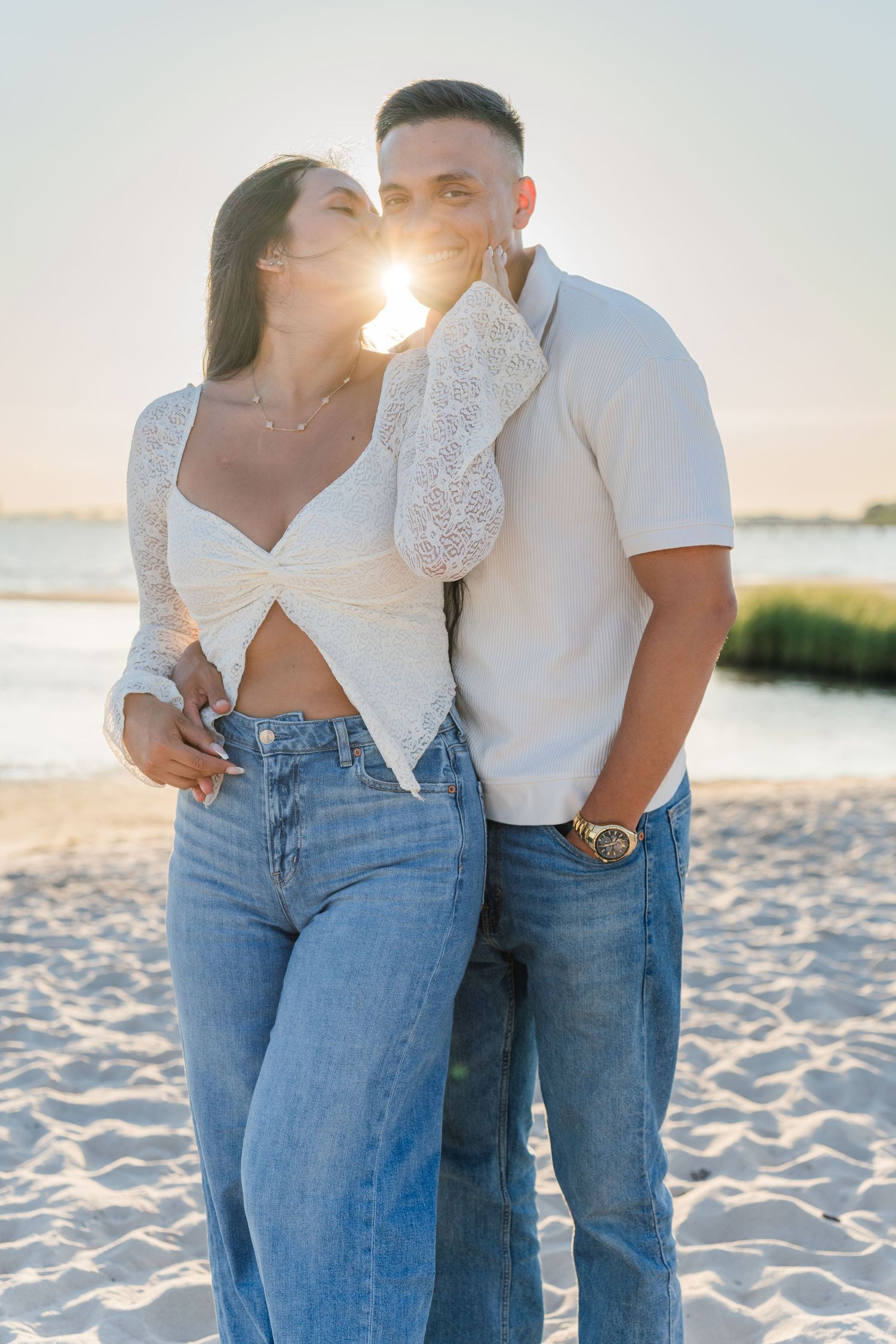 Romantic couple in casual outfits embrace on beach at sunset.