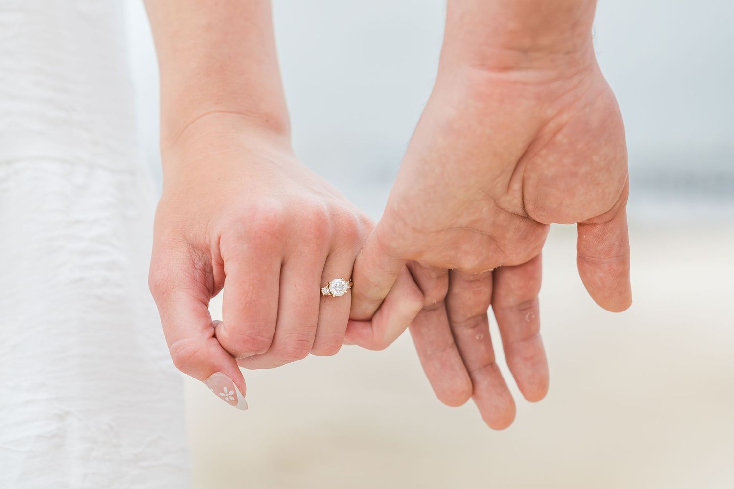 Close-up of a couple holding hands, woman wearing a diamond engagement ring, symbolizing love and commitment.