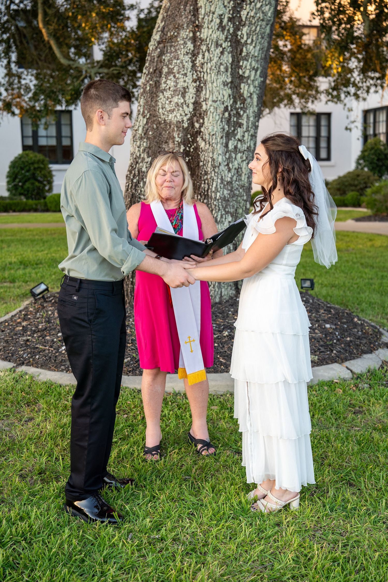 Wedding guests gather for casual photos under mature oak trees at dusk.