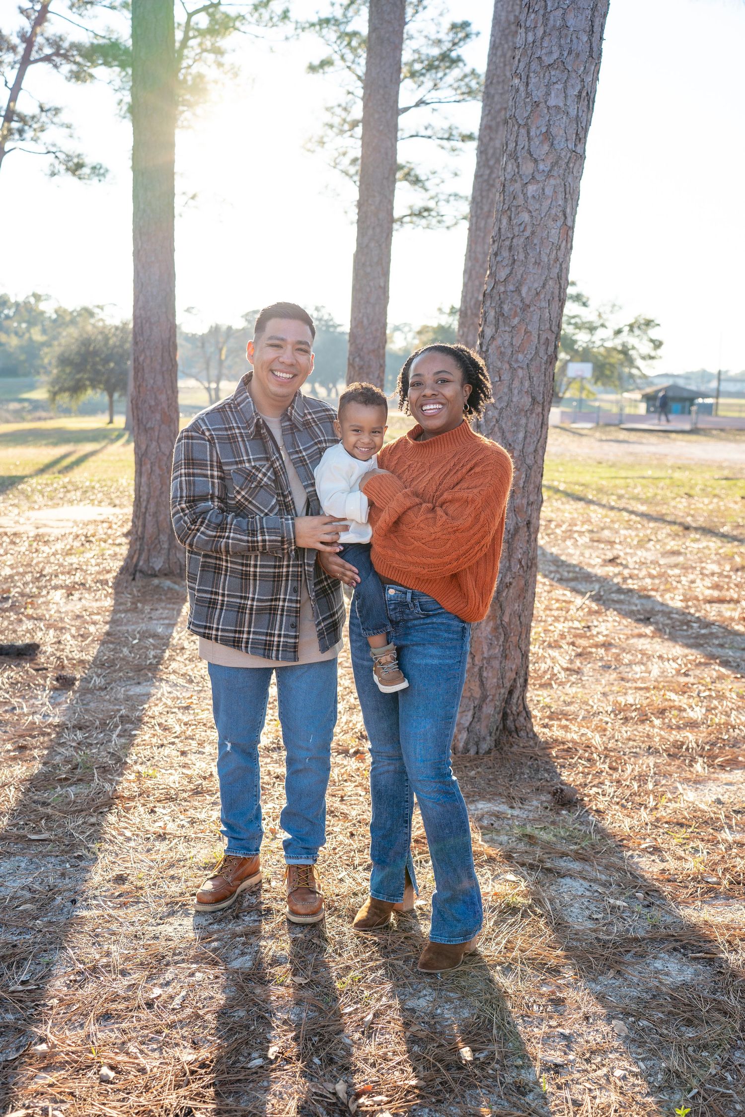 Family walking through pine trees during golden hour with long shadows on fallen leaves.