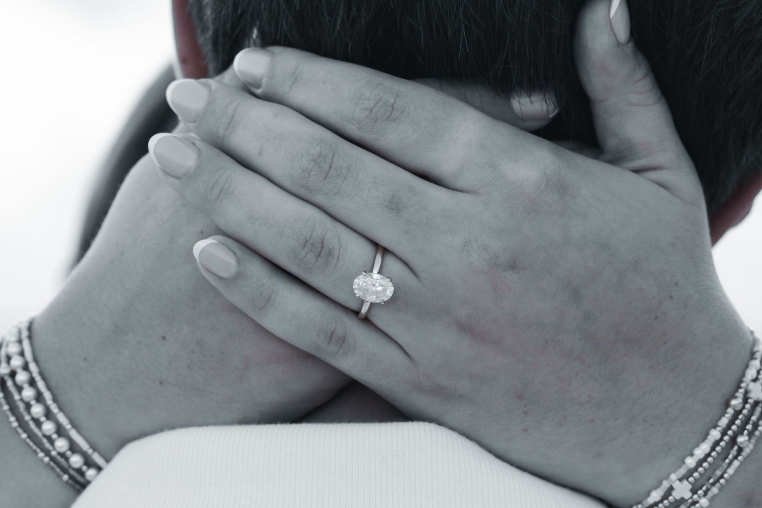 Black and white close-up of hands embracing, featuring a stunning diamond engagement ring and delicate bracelet.