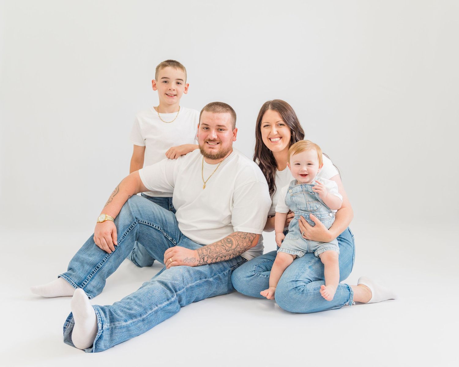 Studio portrait of a family in white tops and jeans against a light background.