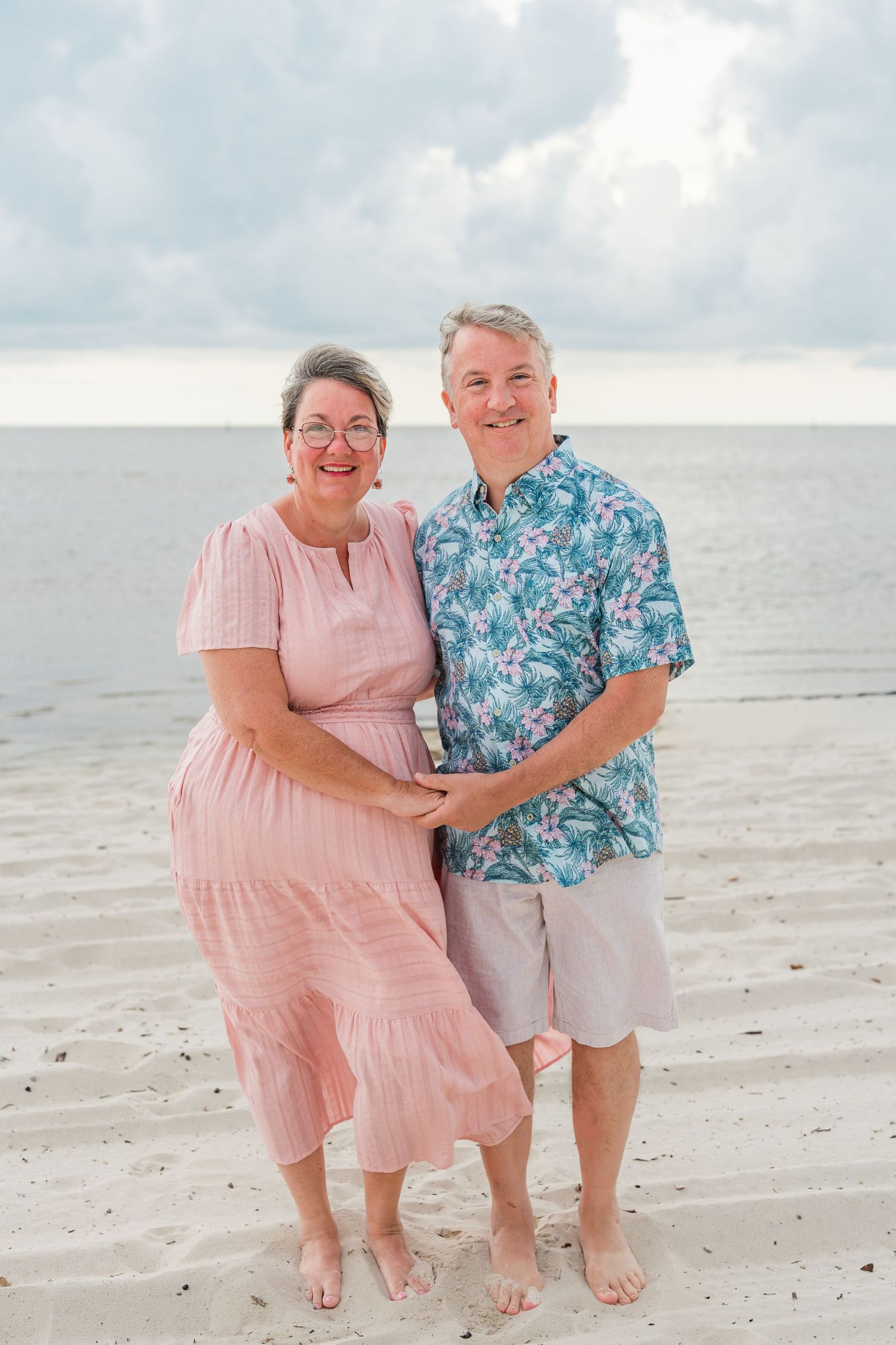 Beach portrait of two people in coordinating summer outfits smiling together.