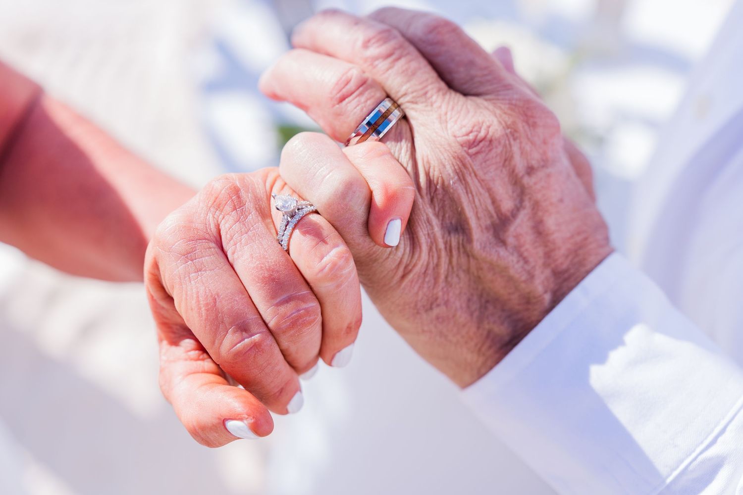 Close-up of hands holding together in a caring gesture against a bright background.