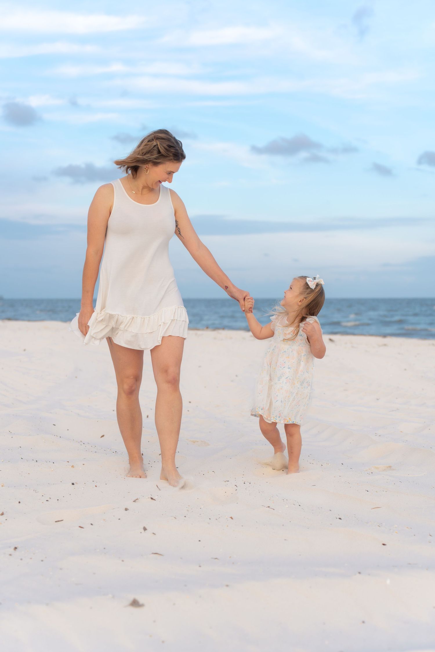 Two people walking hand in hand along a pristine white sandy beach at sunset.