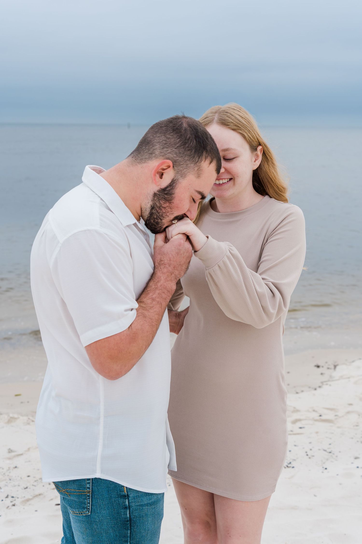 A couple shares intimate moments on a serene beach with white sand and cloudy skies in the background.