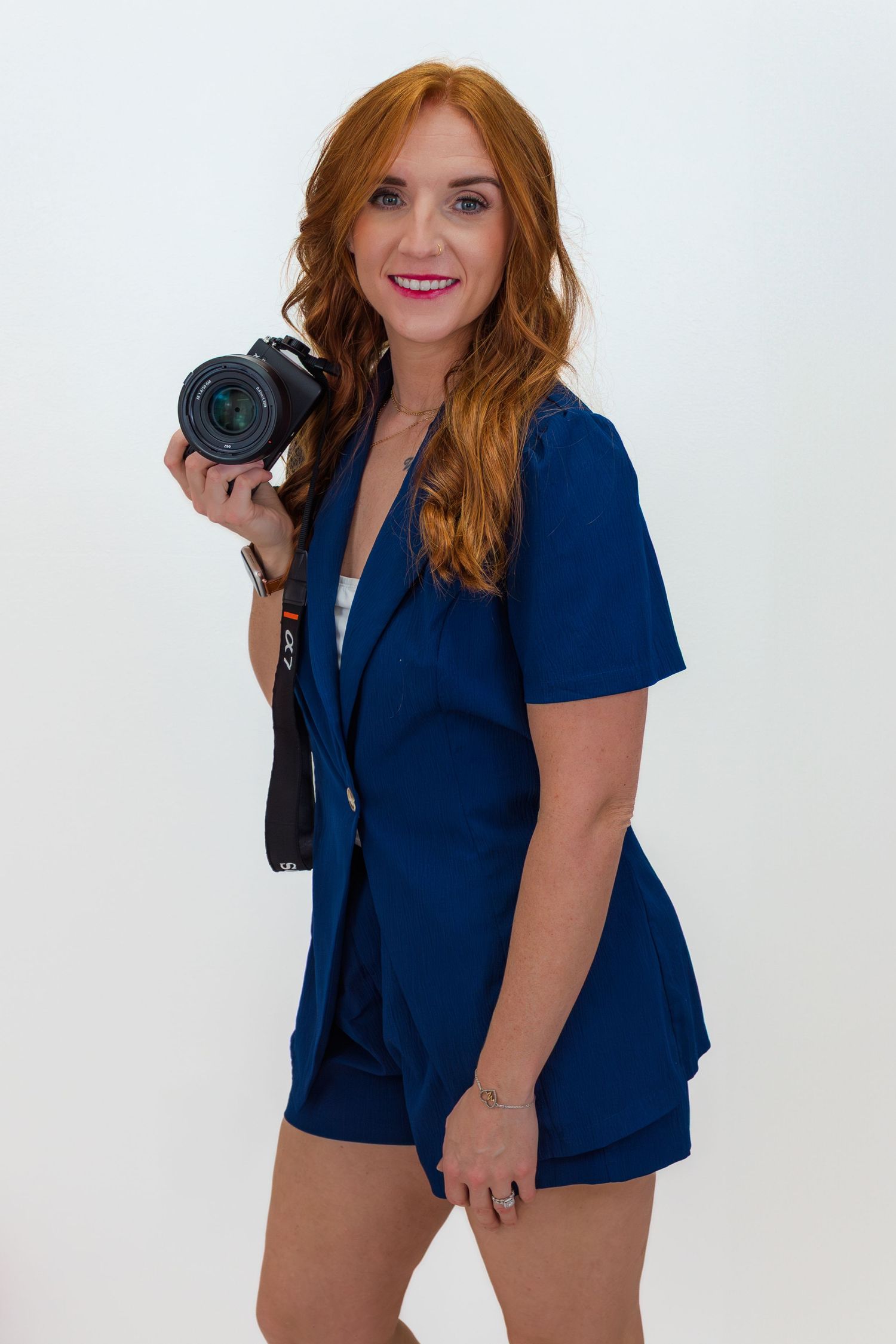 Portrait session in navy blue outfit holding professional camera against white background.