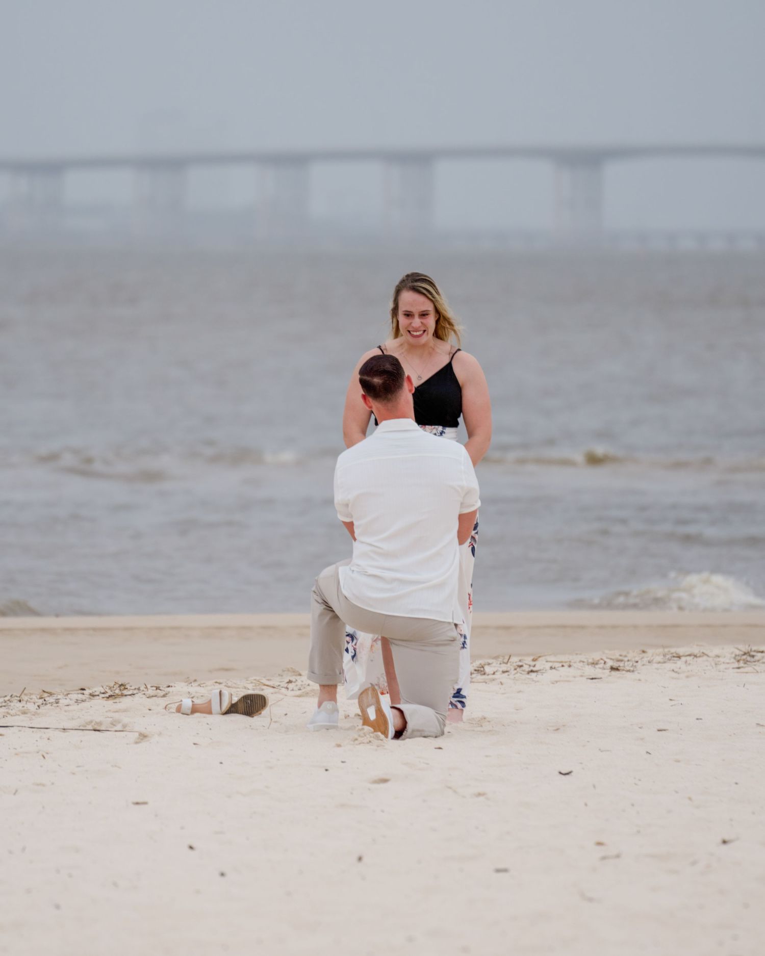 A romantic proposal scene unfolds on a sandy beach with ocean waves in the background.