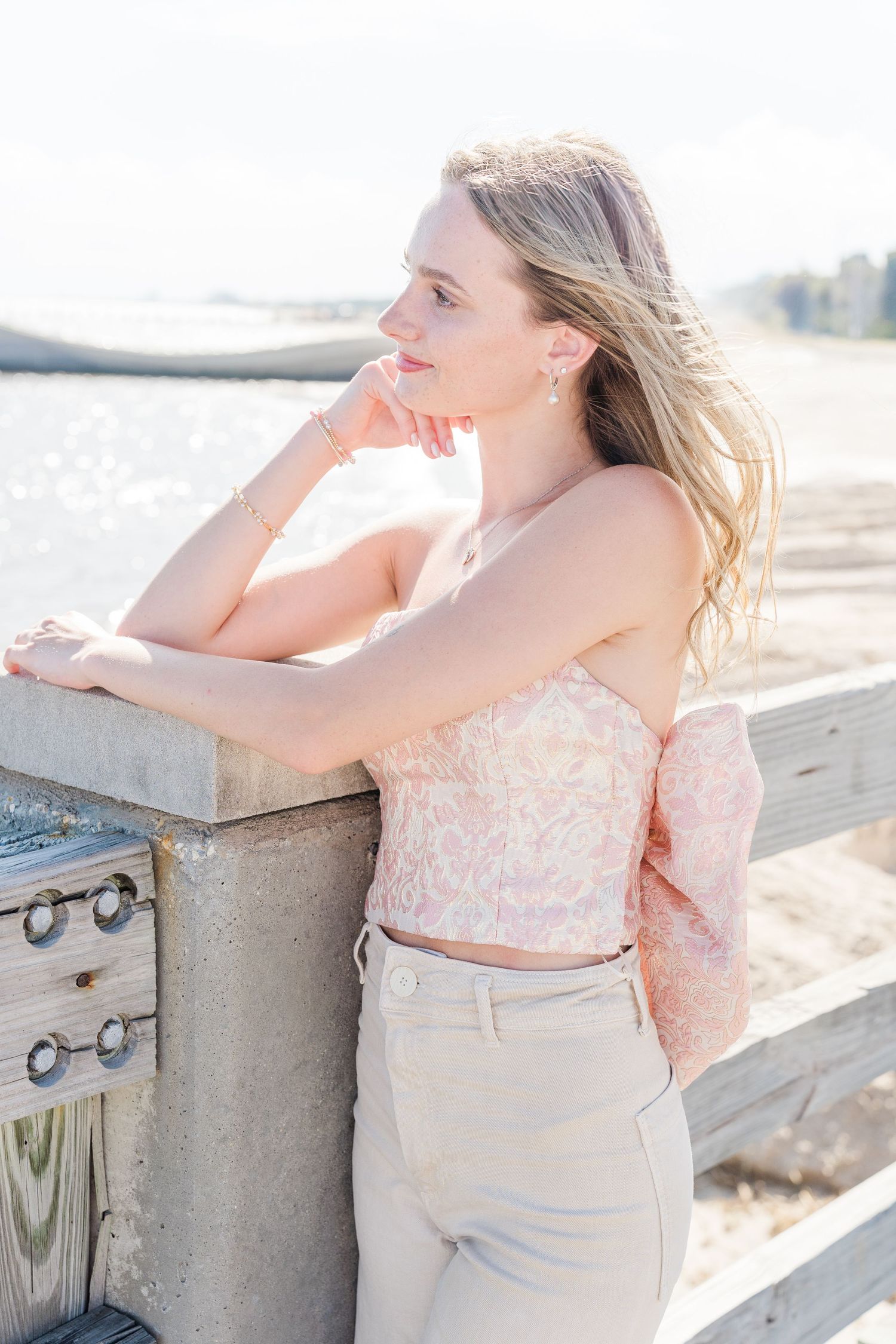 Person in pink top leans on railing by waterfront during sunset.
